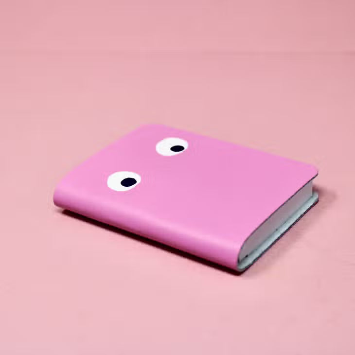 Hot pink mini leather notebook with two white googly eyes on the cover