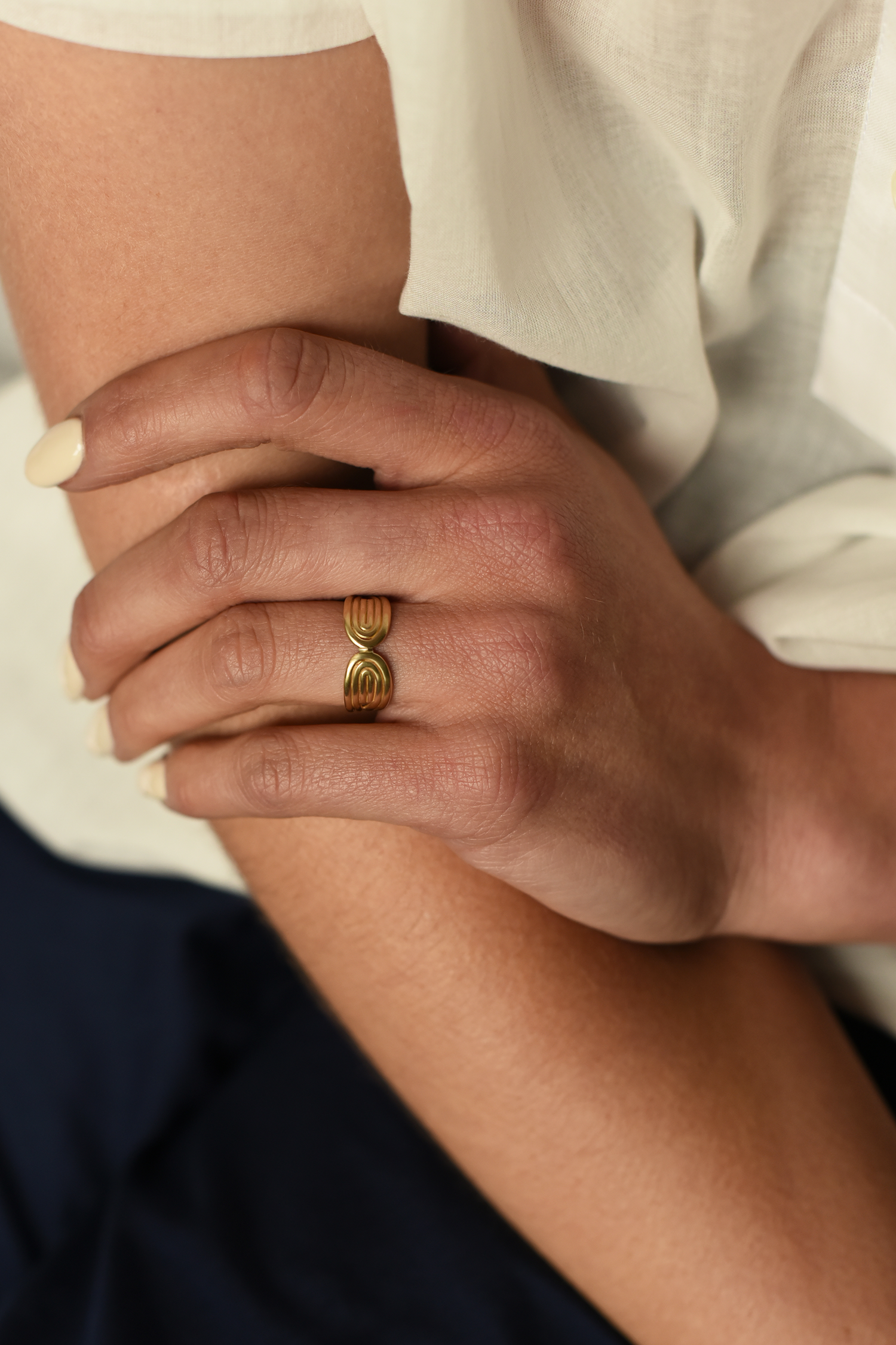 Gold sculpted double-arc ring on finger, stacked oval arcs with spiral motif