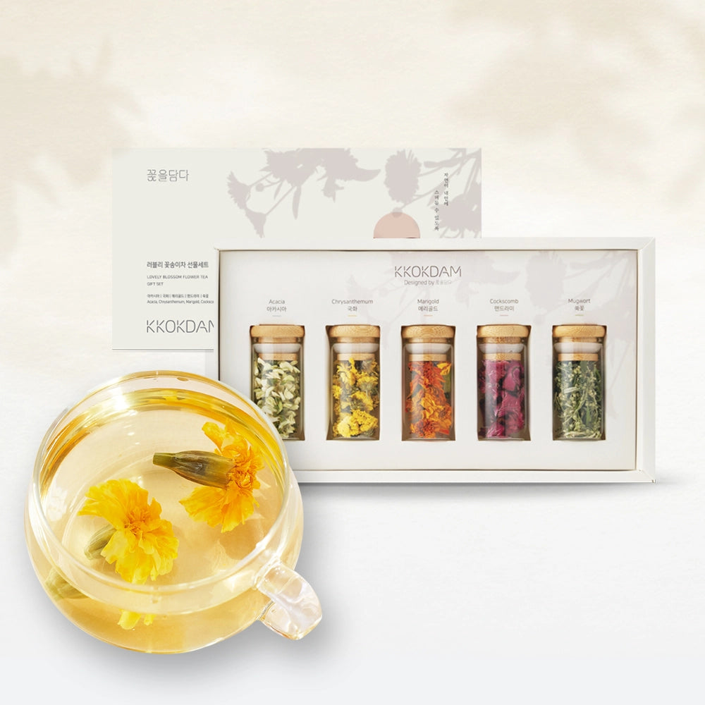 Glass mug of yellow flower tea with dried blossoms beside boxed tea jar set