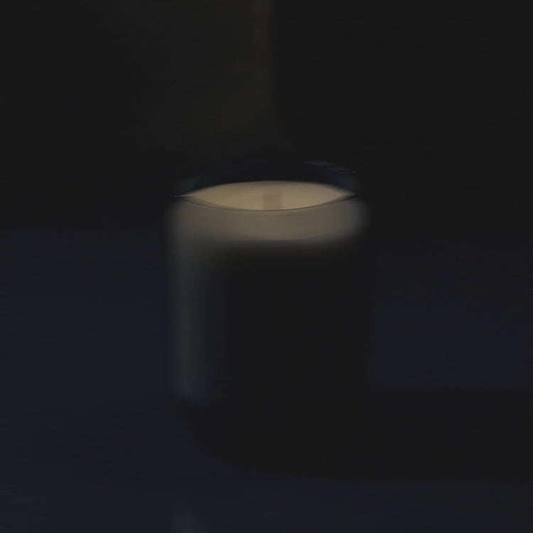 Waxed perfume candle with lit flame in glass jar, softly blurred