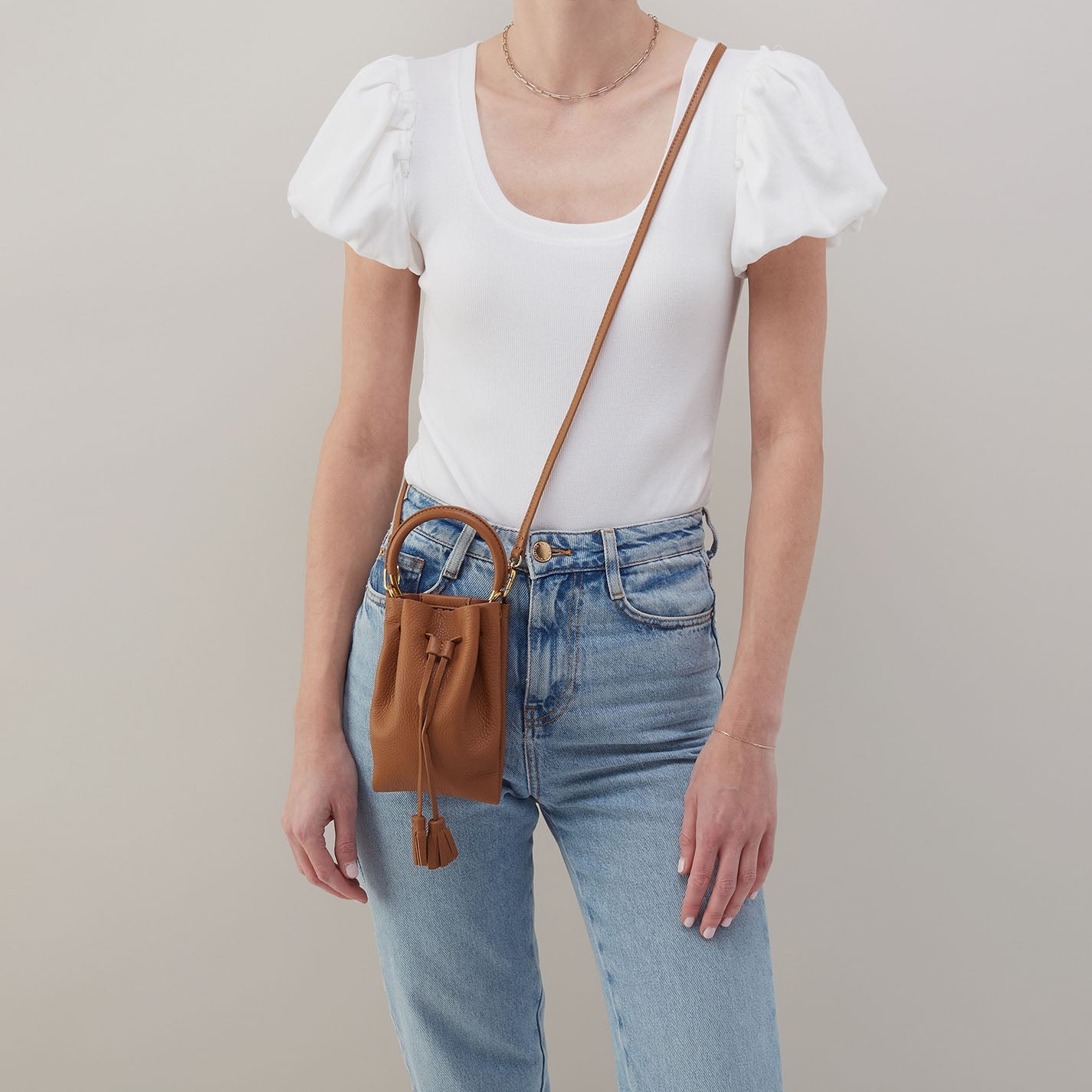 Warm honey phone crossbody bag on model with adjustable strap and tassel charm.