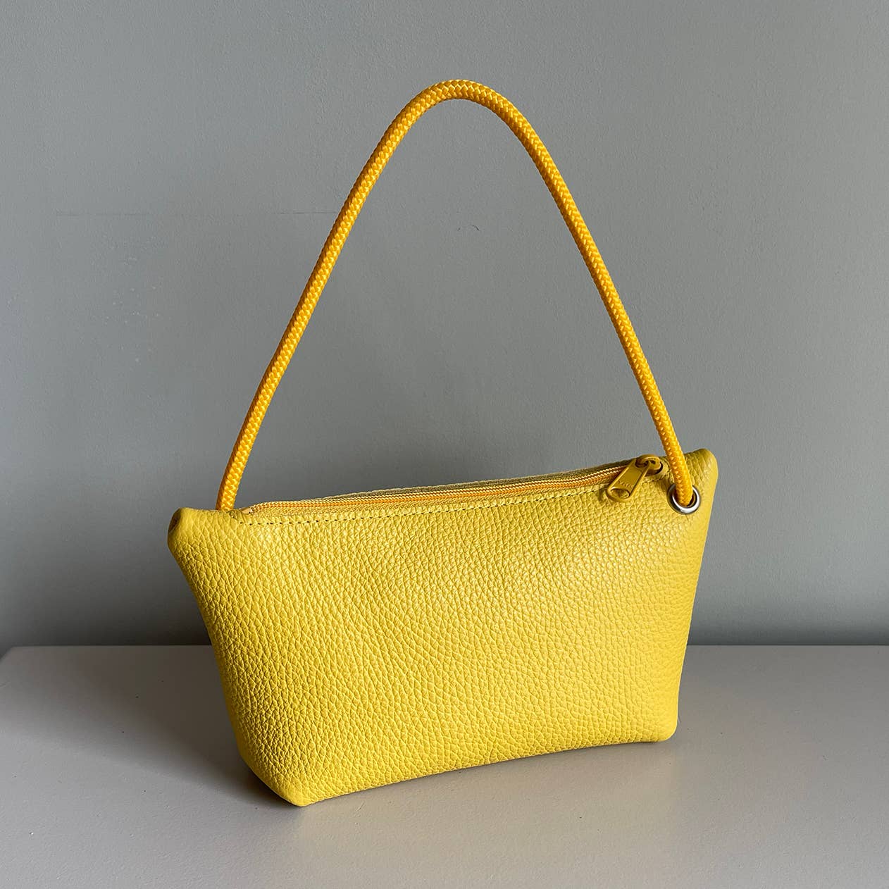 Yellow cord pouch with matching braided handle and smooth leather texture.