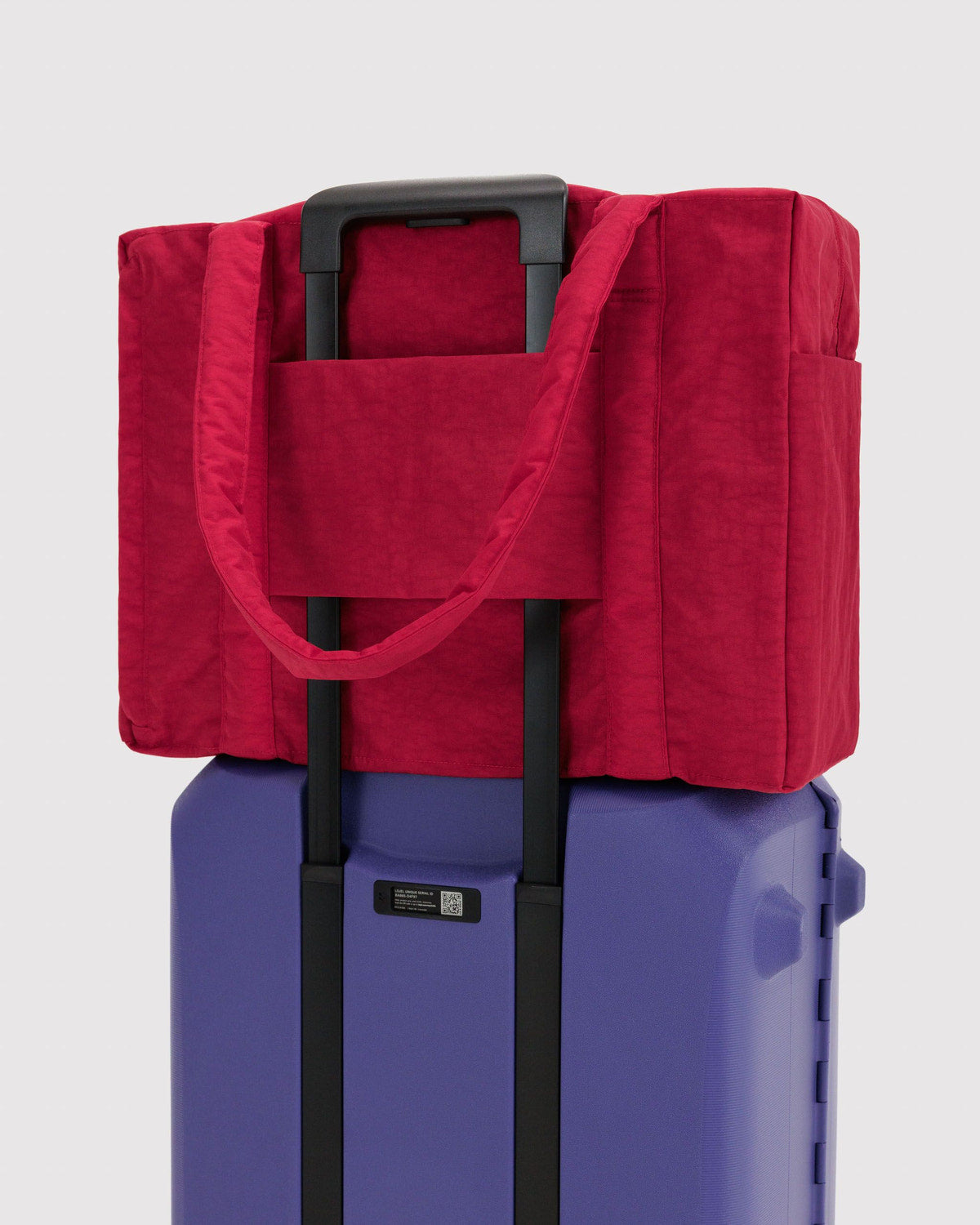 Red carry-on tote bag with front pocket over rolling suitcase