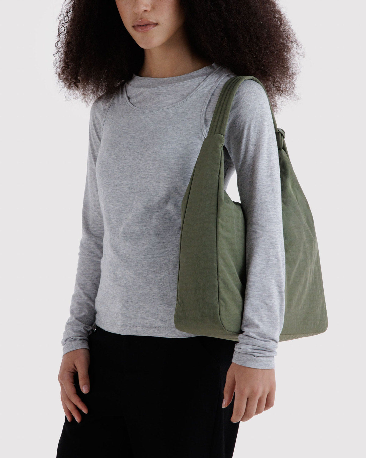 Nylon shoulder bag in olive green worn on shoulder with curved handle and wide strap.