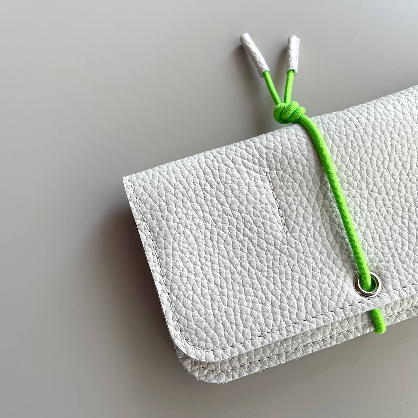 White leather knot wallet with front flap and green cord tie, pebbled leather texture