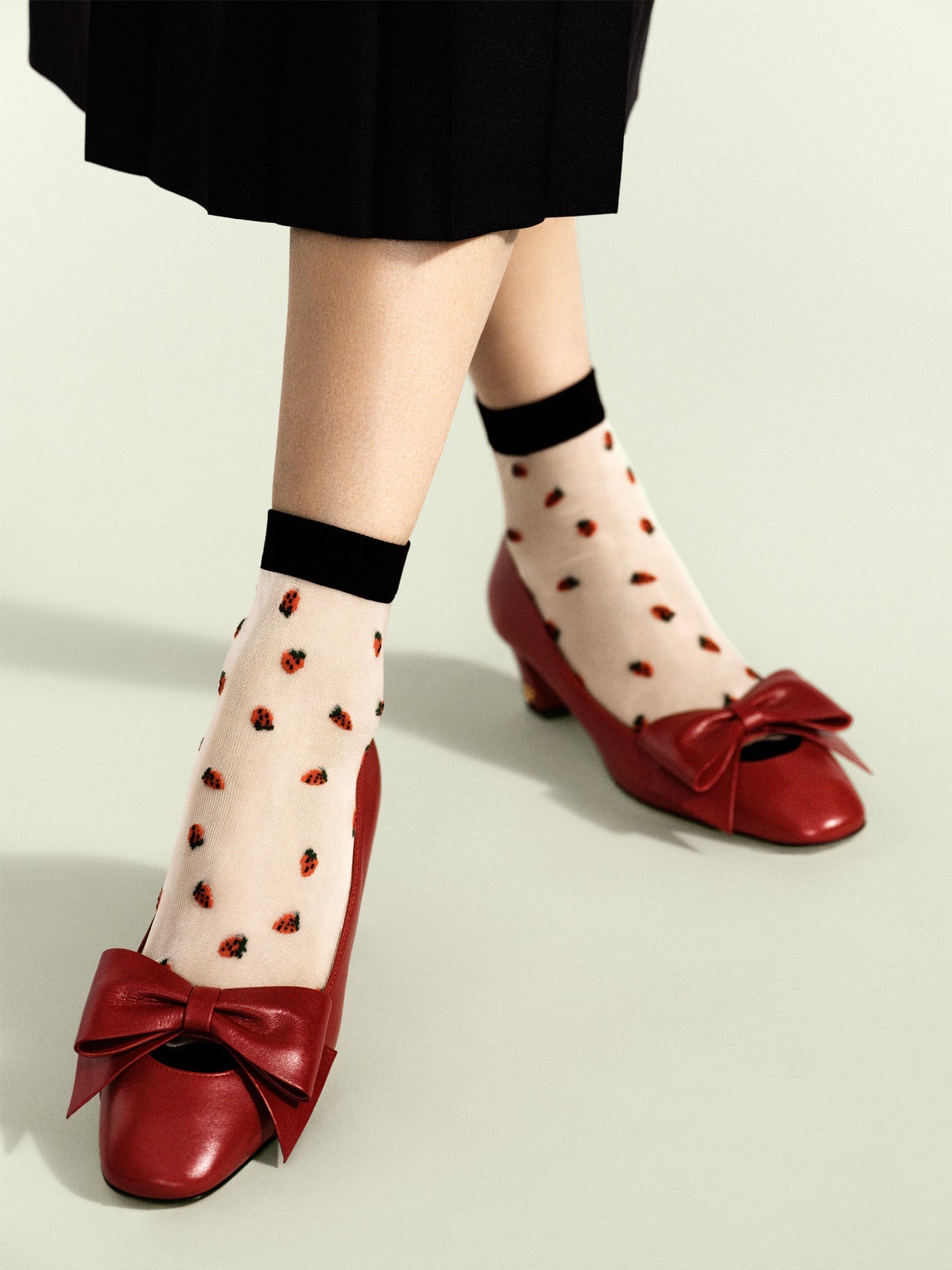 Baby sheer crew socks with black cuffs and strawberry print, worn with red bow shoes