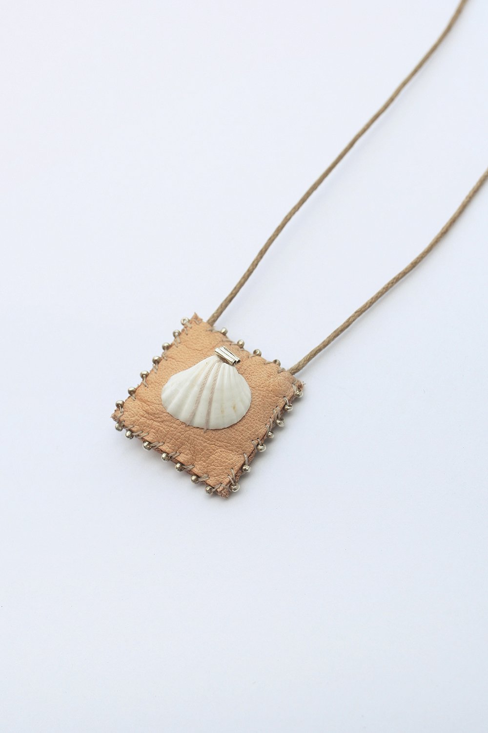 Square seashell pendant close-up with tan backing and bead-like edge, on gold chain