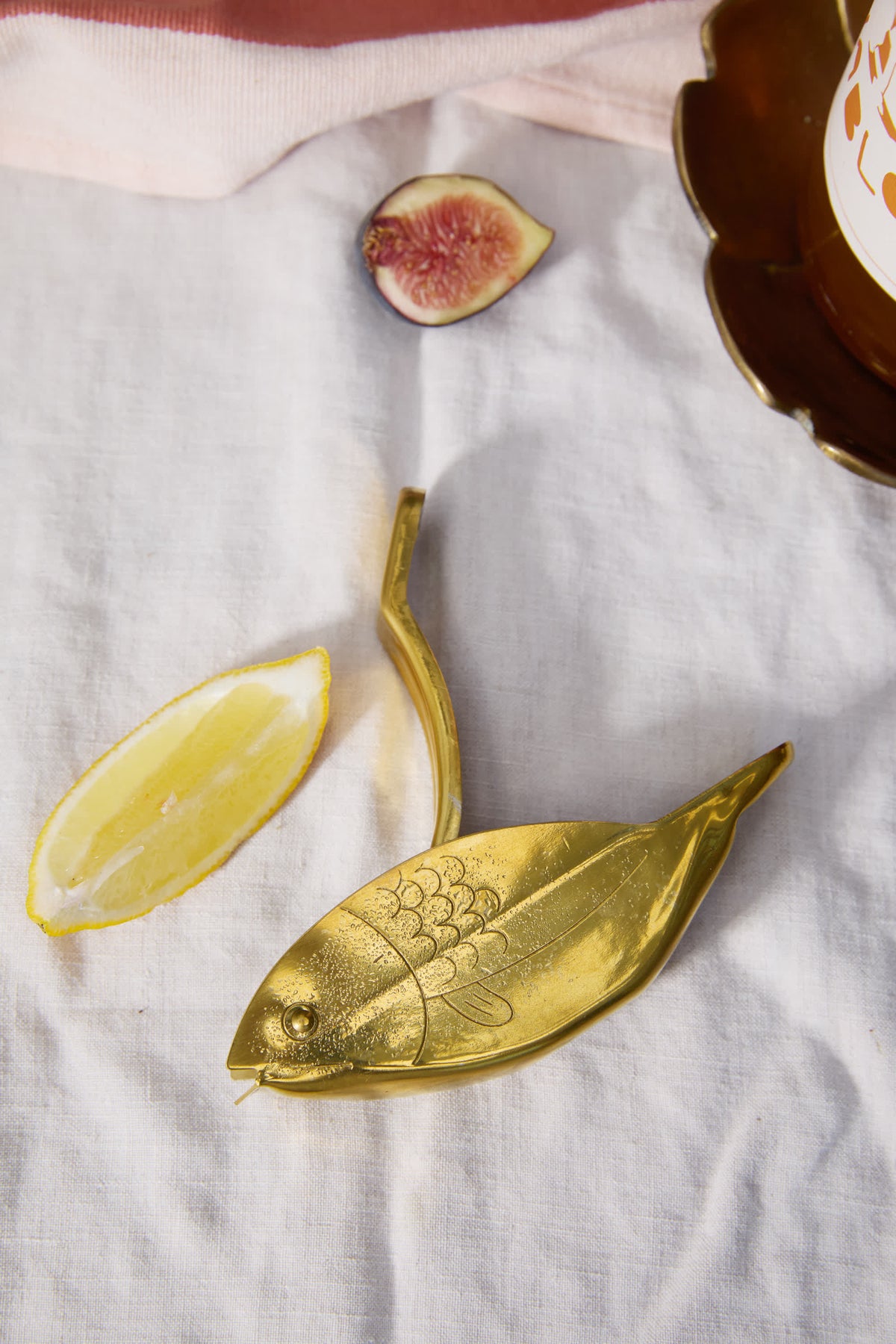 Gold fish citrus juicer with handle, shown near lemon and fig on cloth.