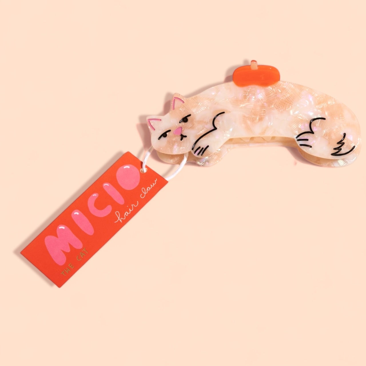 Cream cat hair claw with orange clip, showing cartoon face and hanging tag