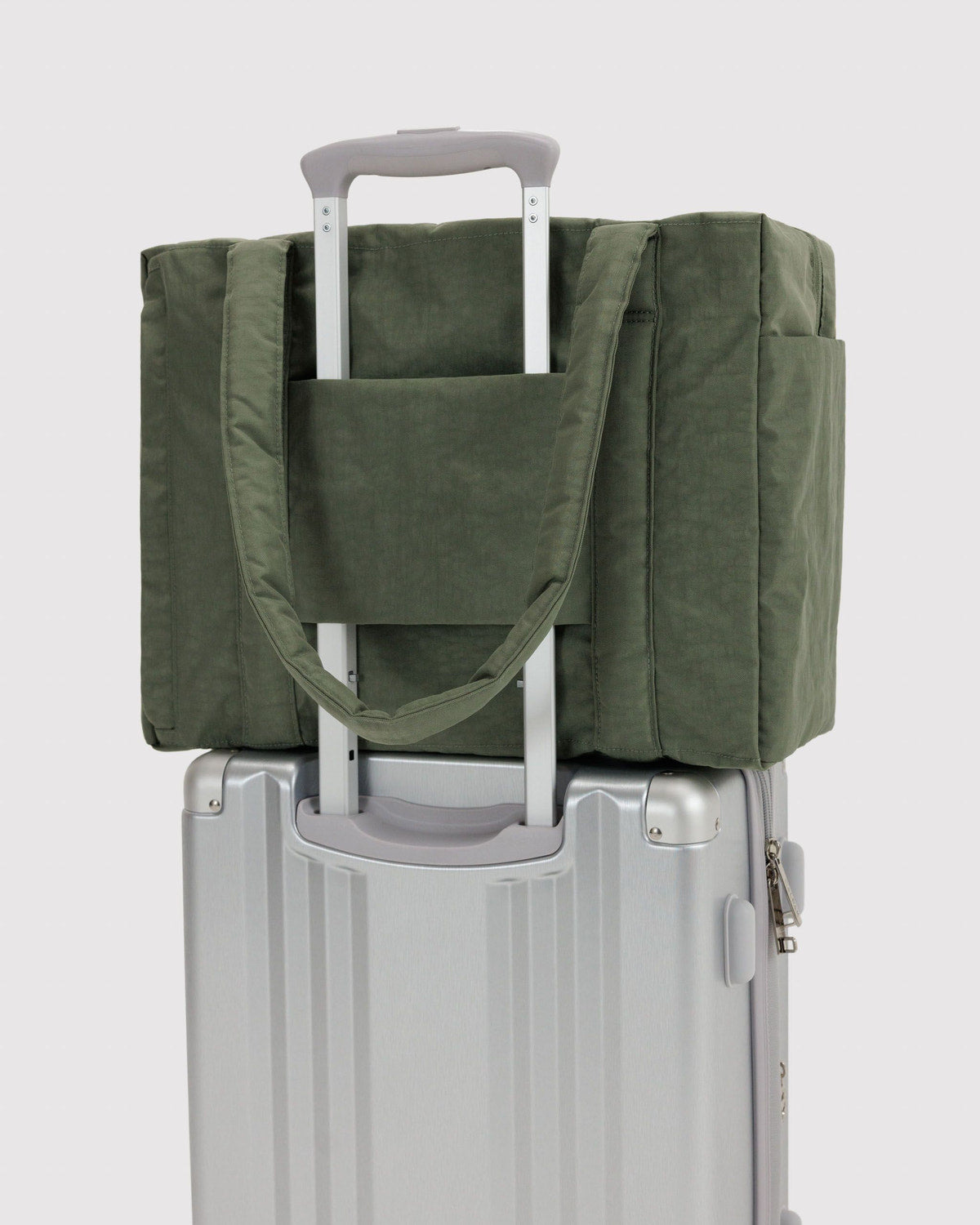 Olive green tote bag attached to a rolling suitcase via luggage strap.