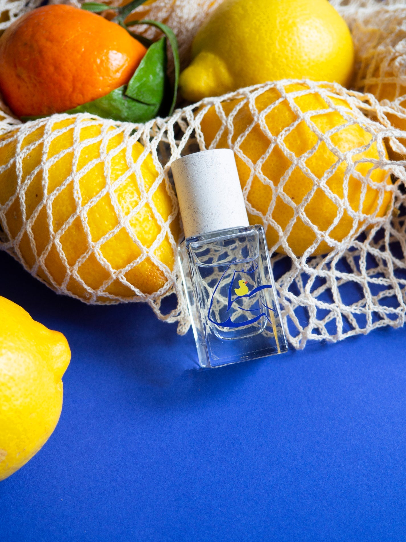 Small clear perfume bottle with white textured cap and blue logo on blue fabric