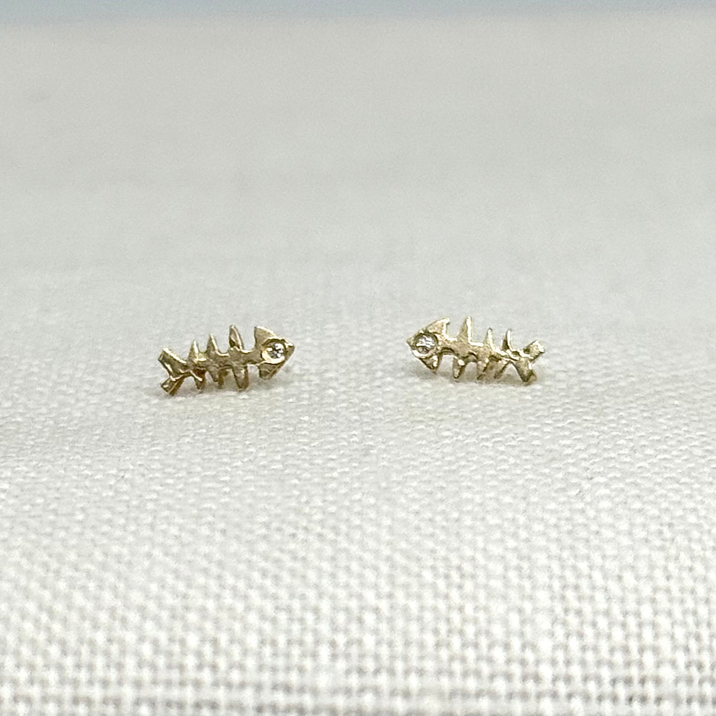 Gold fishbone stud earrings with clear stone accents, curved fish skeleton shape, pair
