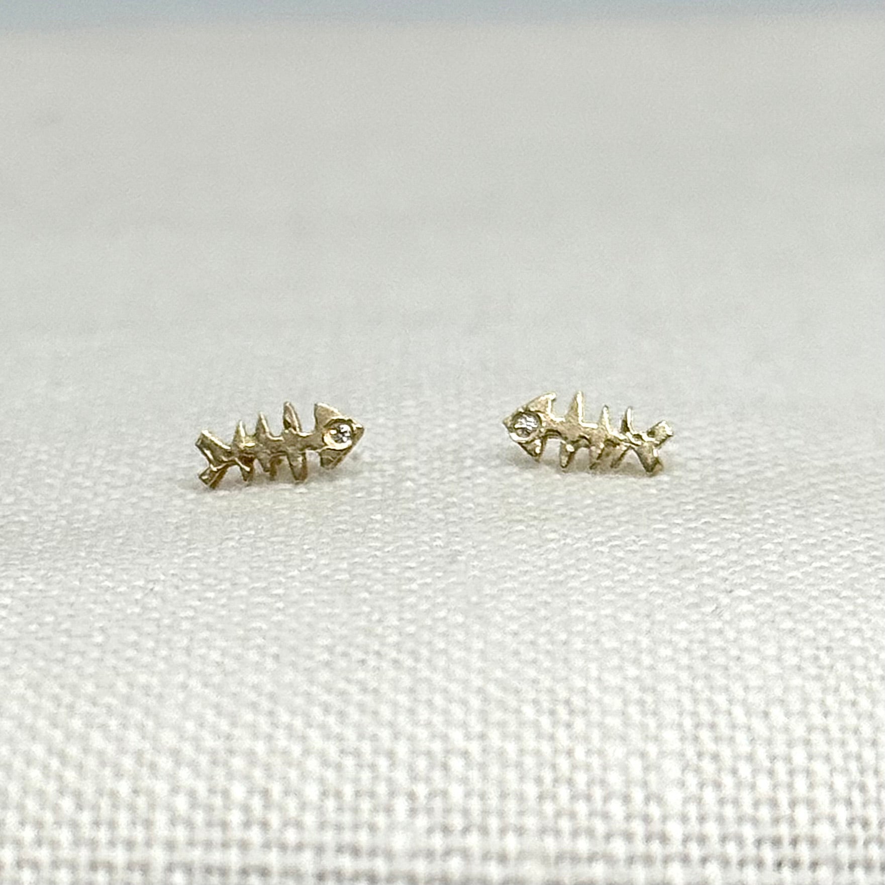 Gold fishbone stud earrings with clear stone accents, curved fish skeleton shape, pair
