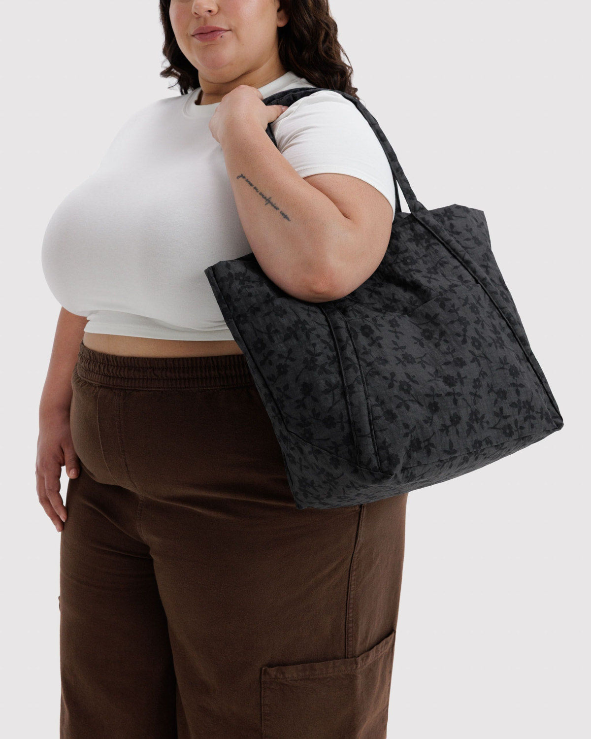 Dark floral tote bag held by a person, showing two top handles and roomy top.