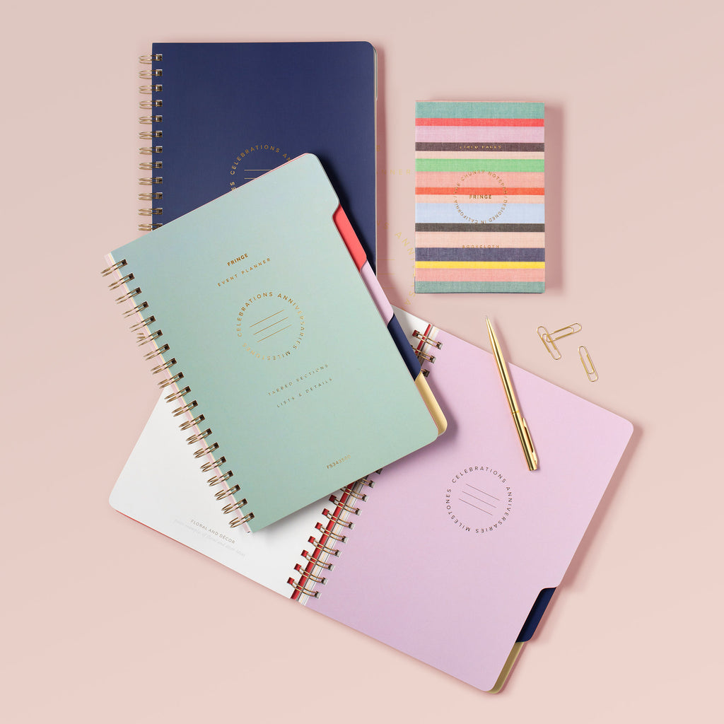 Color-block spiral event planners in sage, navy, and pink with gold ring binding