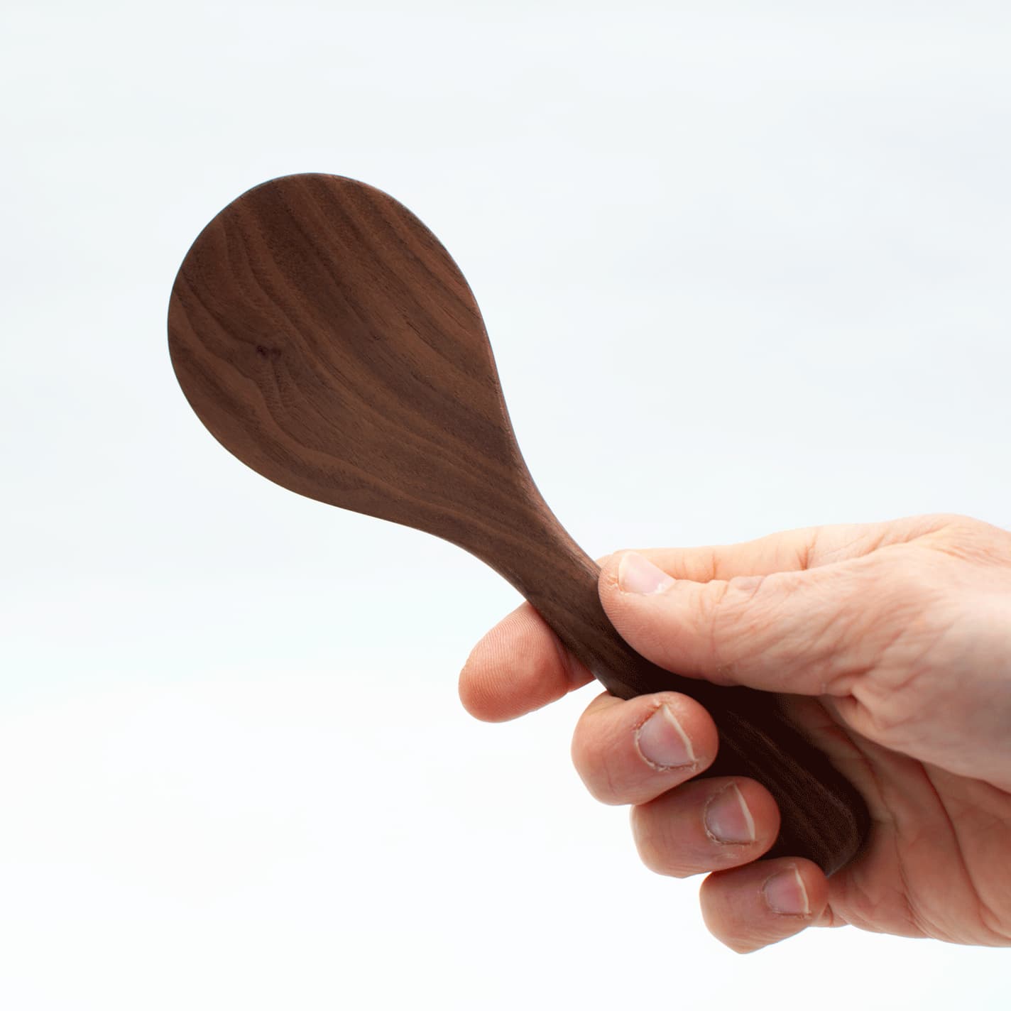 Walnut wood rice paddle held in hand, rounded scoop with smooth finish