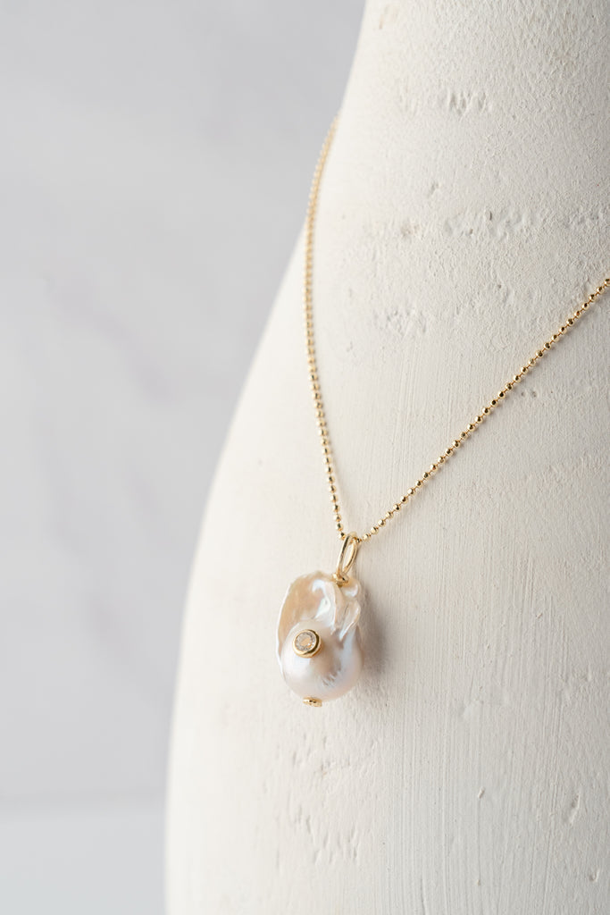Baroque white pearl pendant with topaz-like center detail on gold chain.