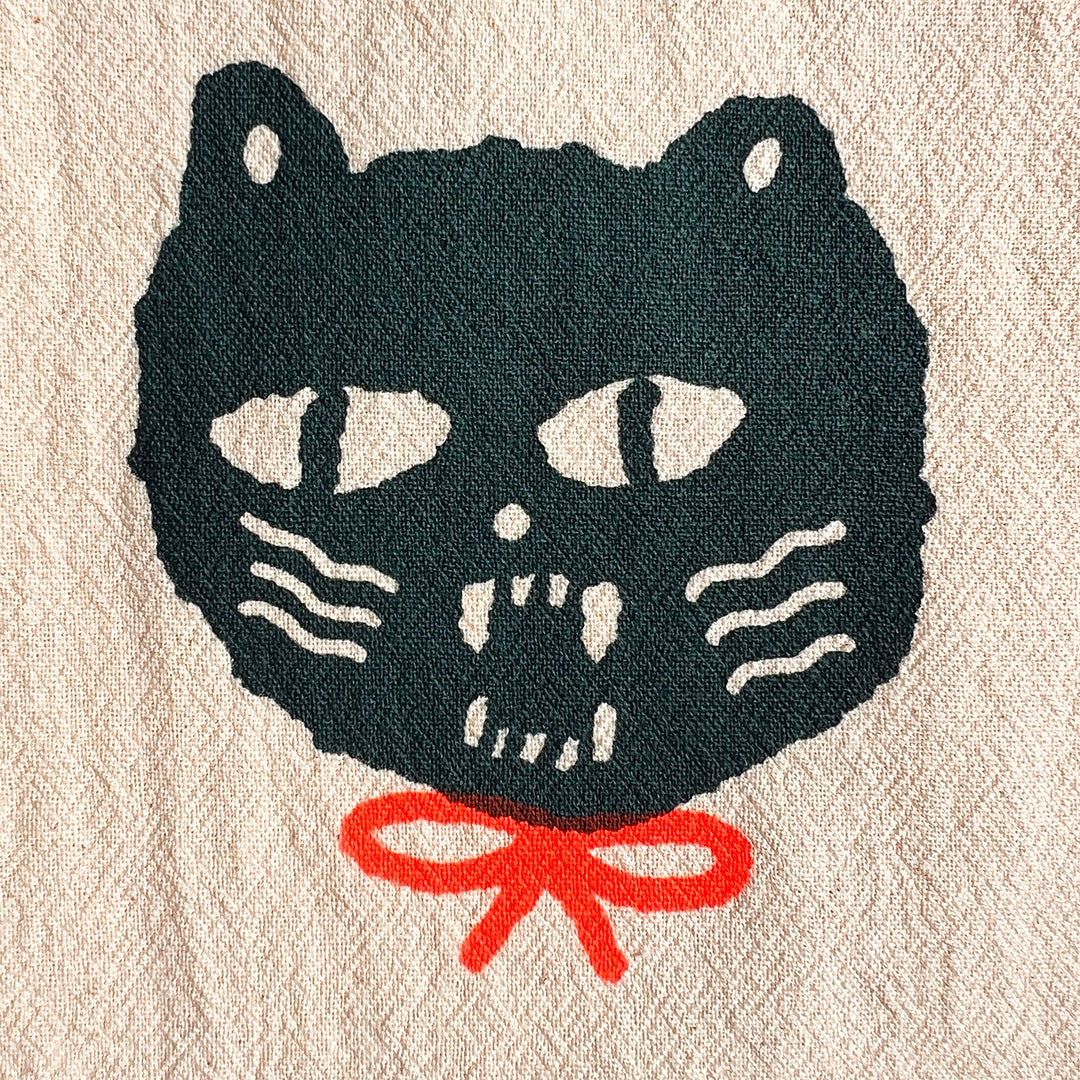 Close-up tea towel featuring dark cat face illustration with red bow