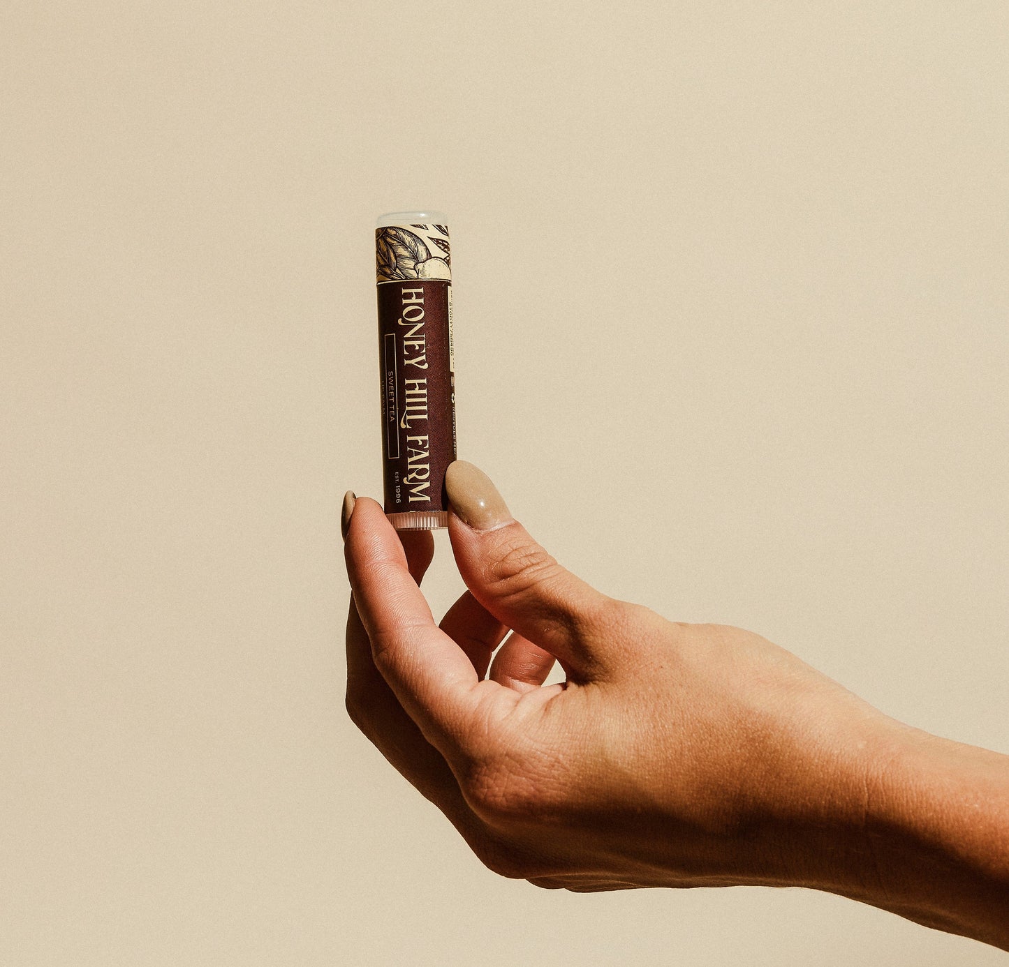 Lip balm tube held in hand, brown label with white cap