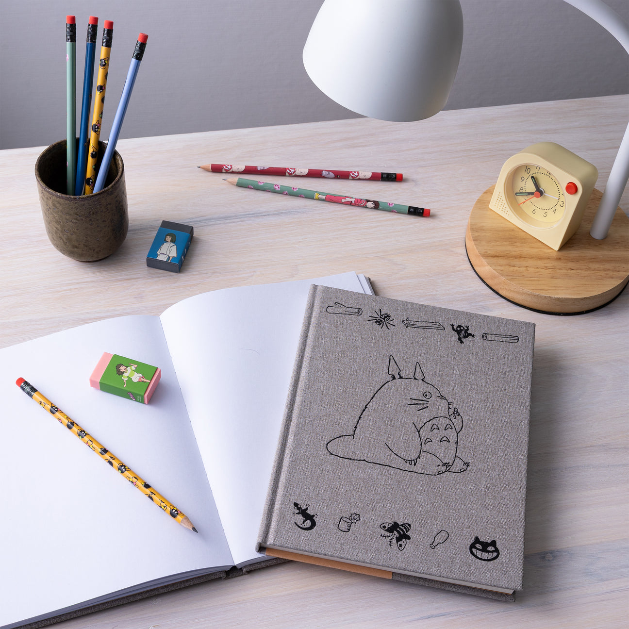Sketchbook open with gray cover showing Totoro-style cat line art, angled view.