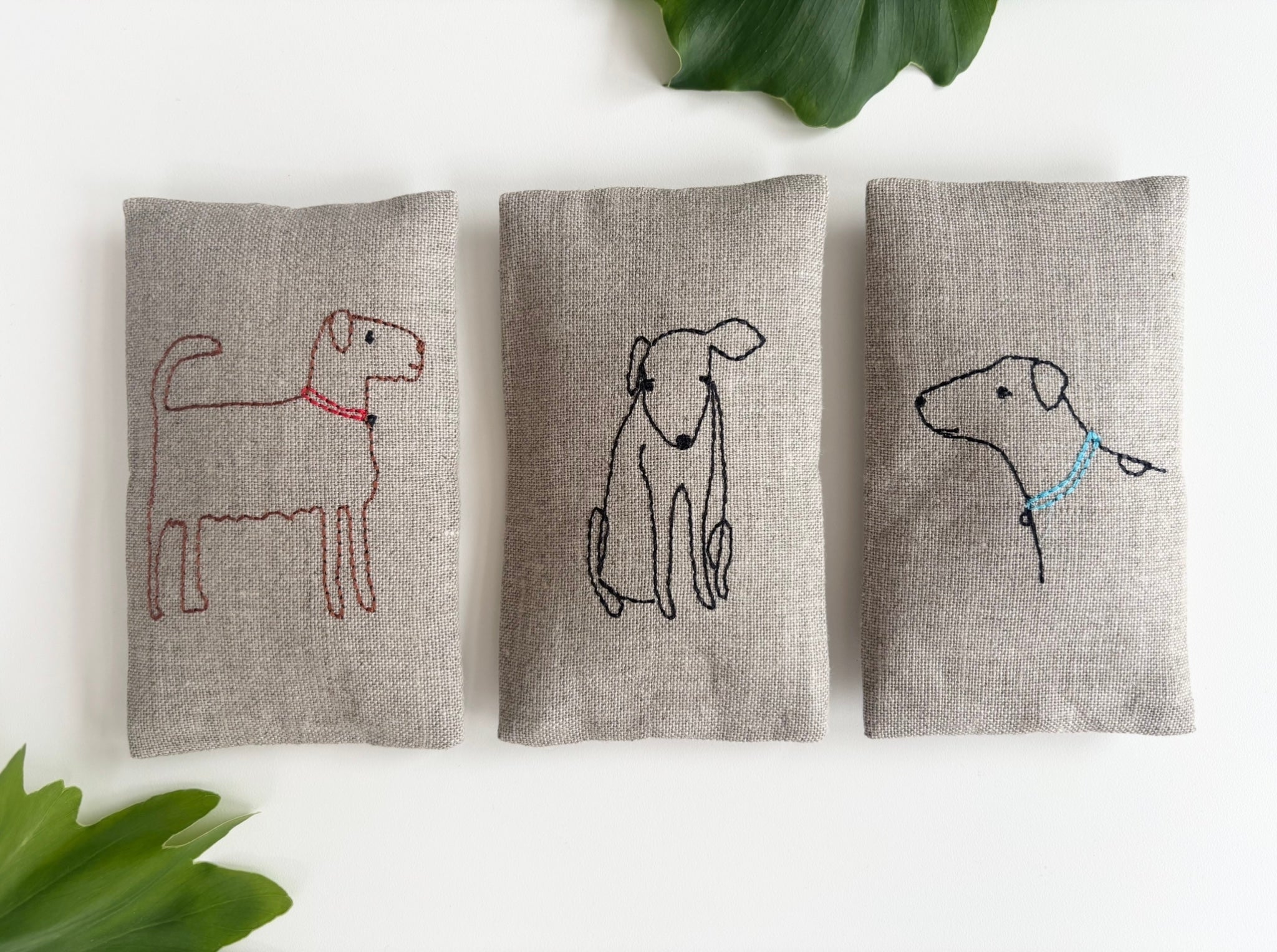 Set of three gray fabric sachet pouches with outlined dog embroidery in red, blue, and black
