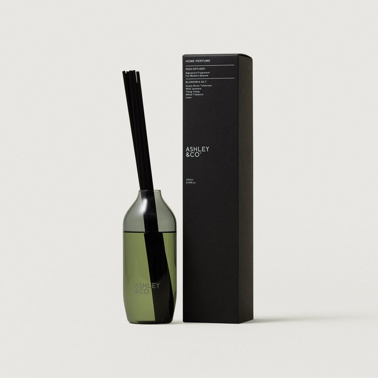 Green glass reed diffuser bottle with black reeds beside rectangular black box