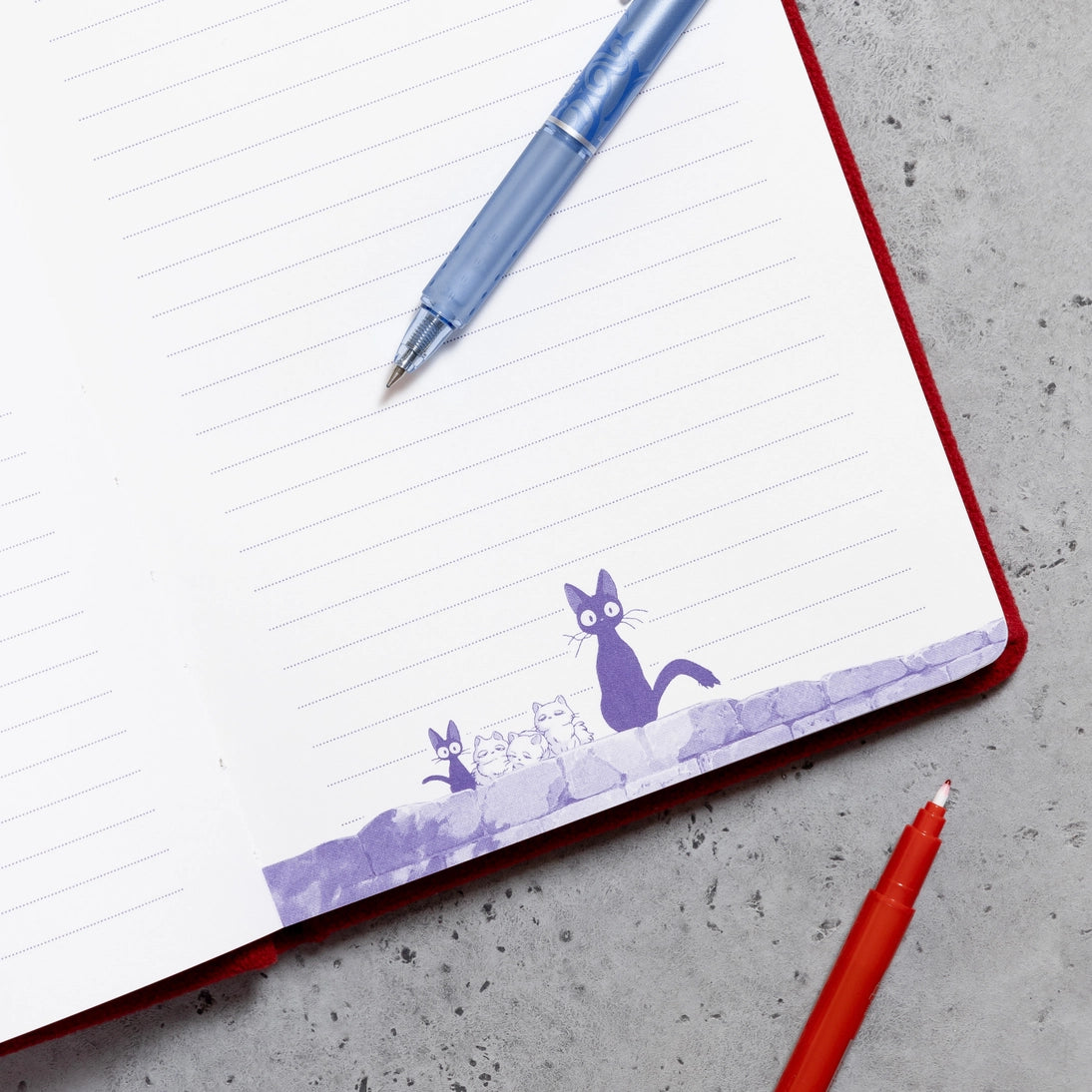 Plush journal page with purple cat illustration on lined paper beside pens