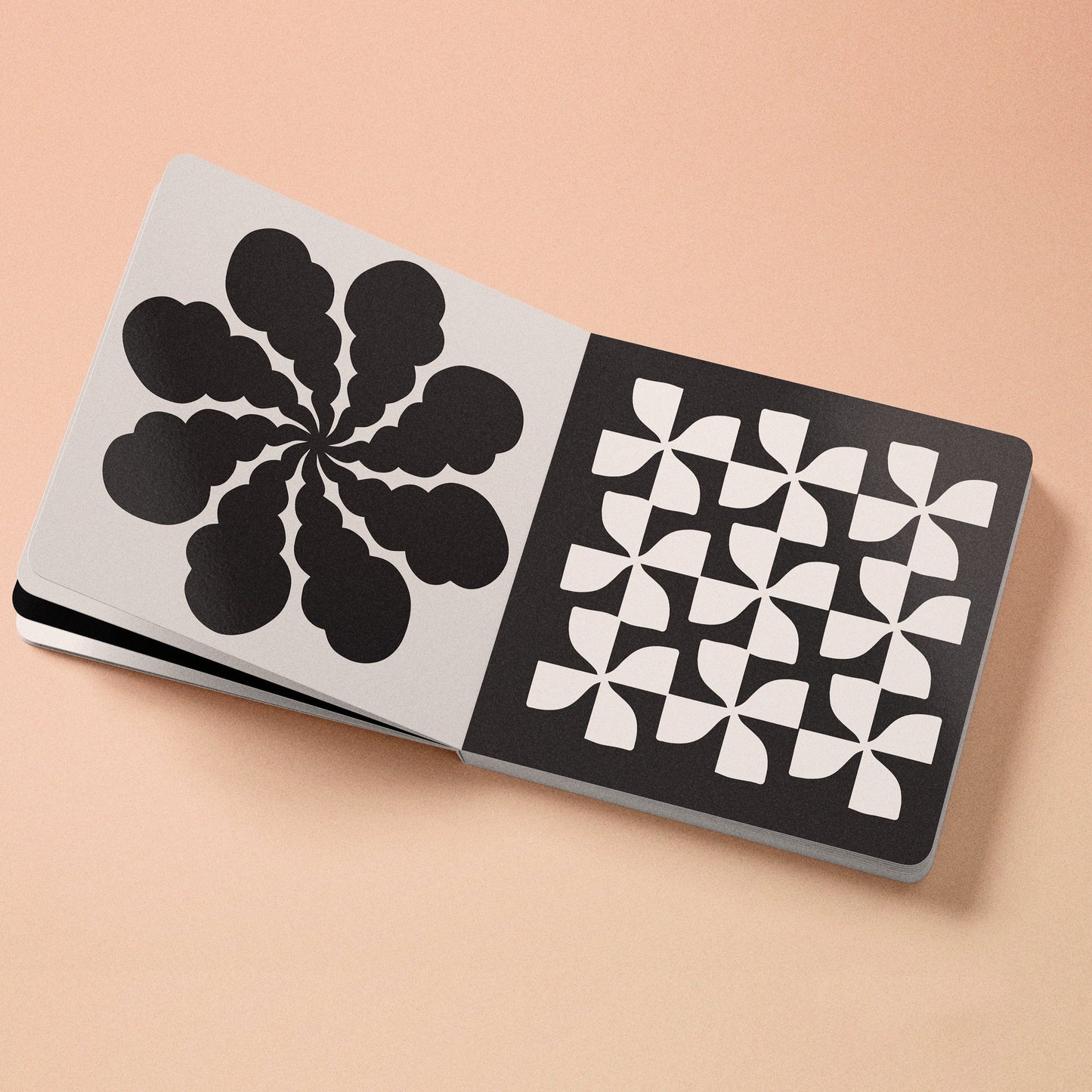 High-contrast baby board book open, black-and-white flower icon and checkered patterns