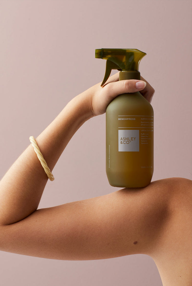 Amber cleanser spray bottle with trigger held near an arm and hand