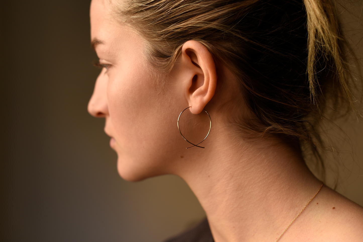 Large round threader earrings on ear, gold-tone hoops with curved wire drop