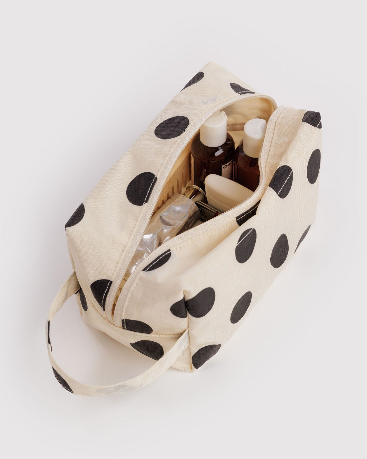 Cream dopp kit with black polka-dot print, open zip reveals bottles and compartments