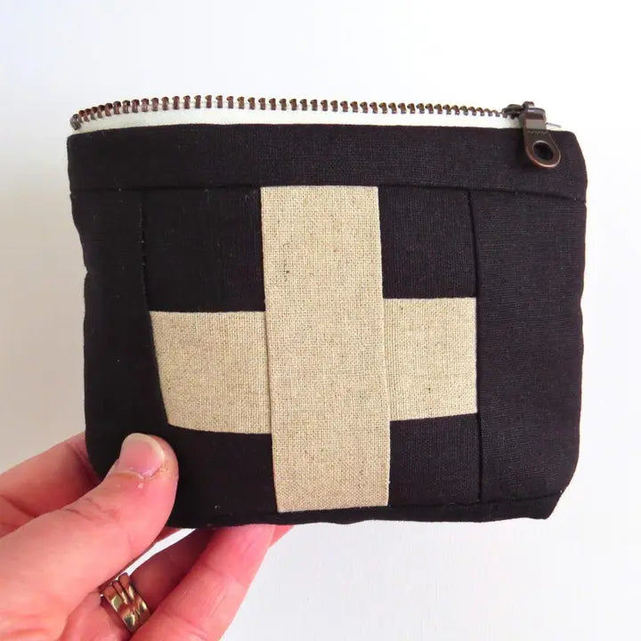 Black first aid kit pouch with cream cross patch and zipper; held by hand