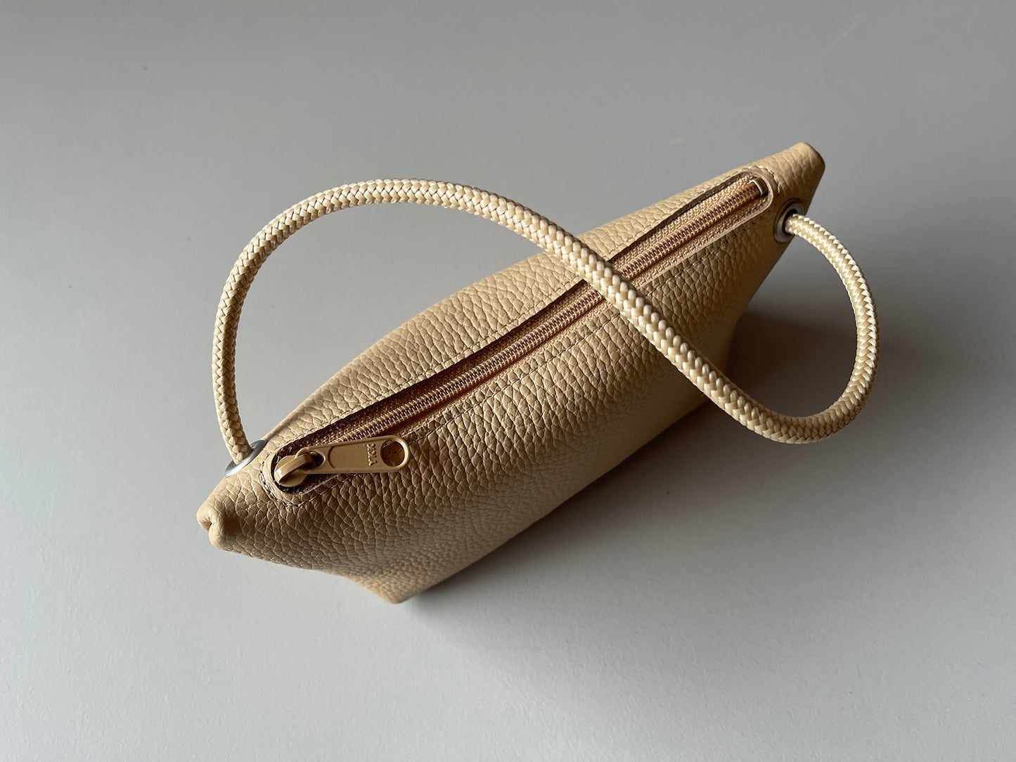 Champagne cord pouch close-up with zipper body and braided loop handle.