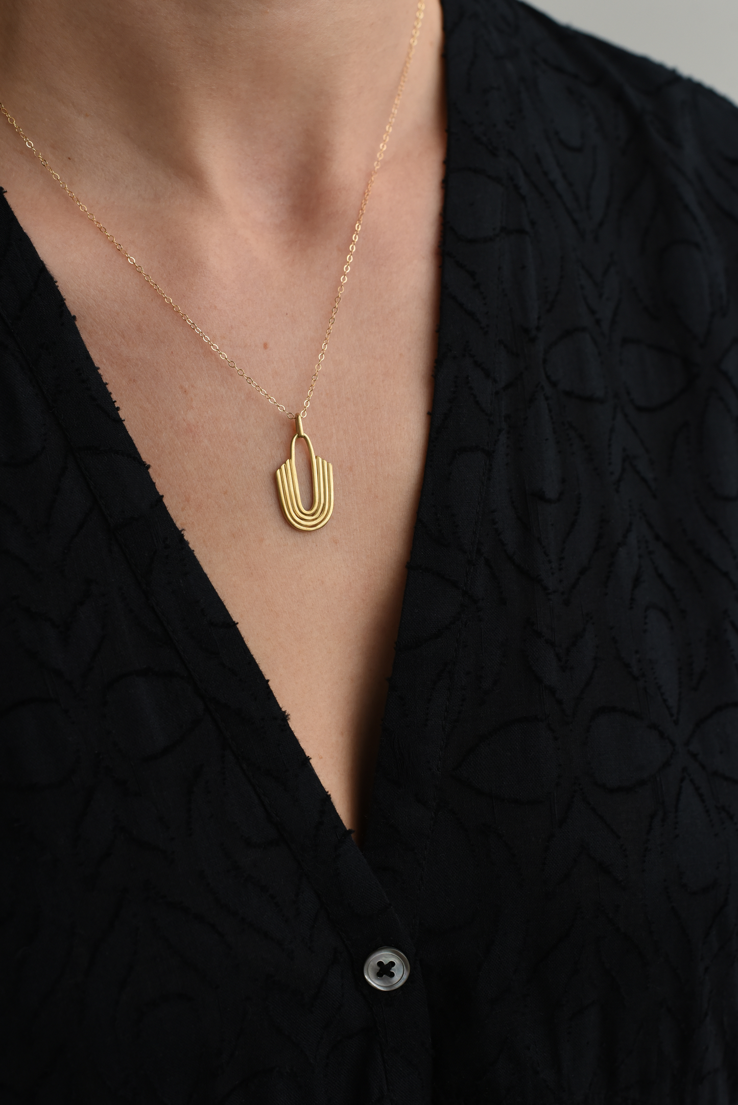Gold U-shaped layered brass pendant necklace on fine chain, worn at the neckline