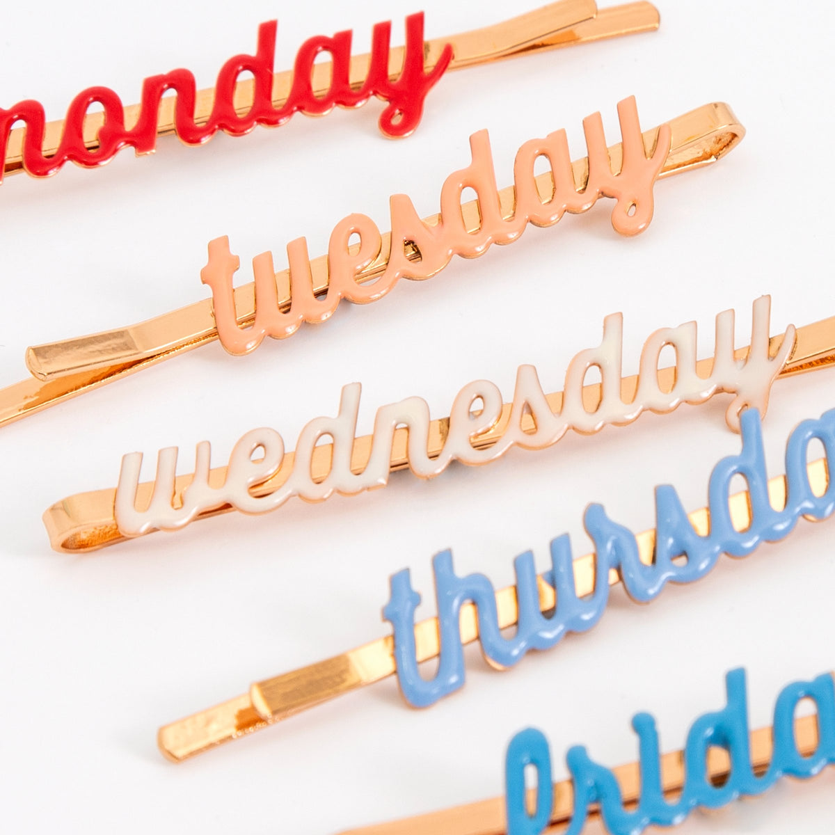 Close-up of enamel weekday hair slides: gold clips with raised 'Monday' and 'Wednesday' text