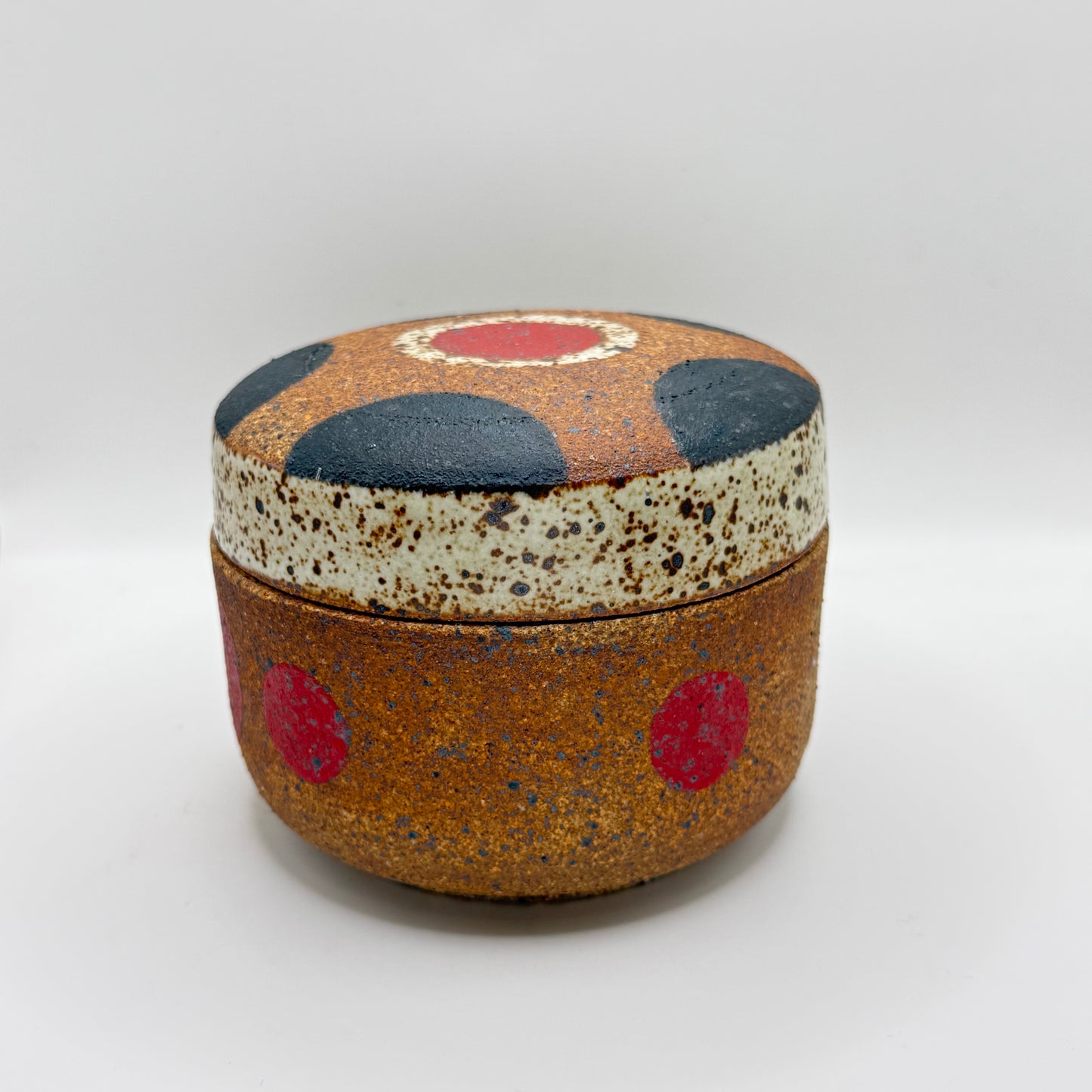 Lidded speckled jar with navy and red dot pattern, orange-brown body
