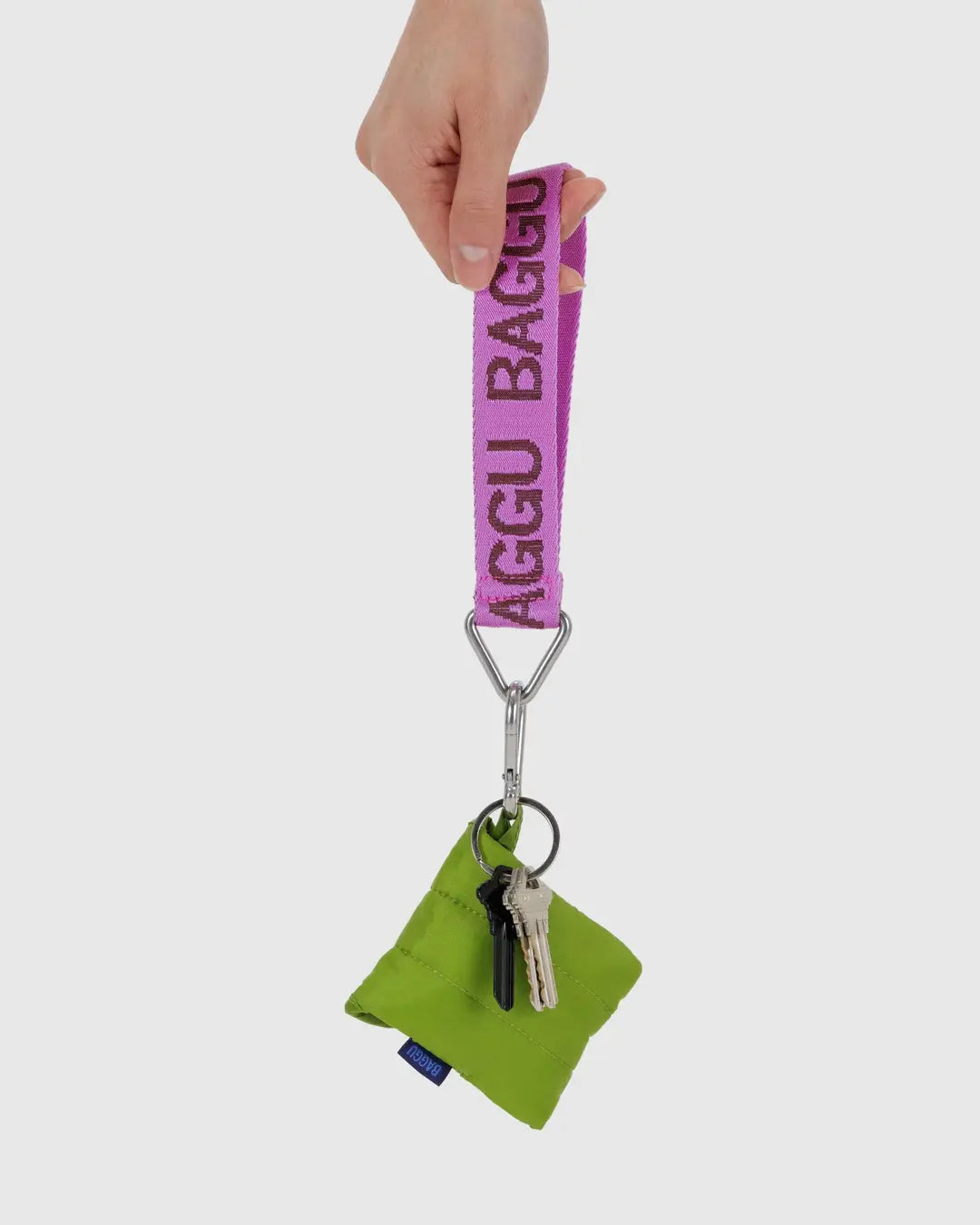 Purple BAGGU logo keychain with green pouch and silver keyring, hand holding