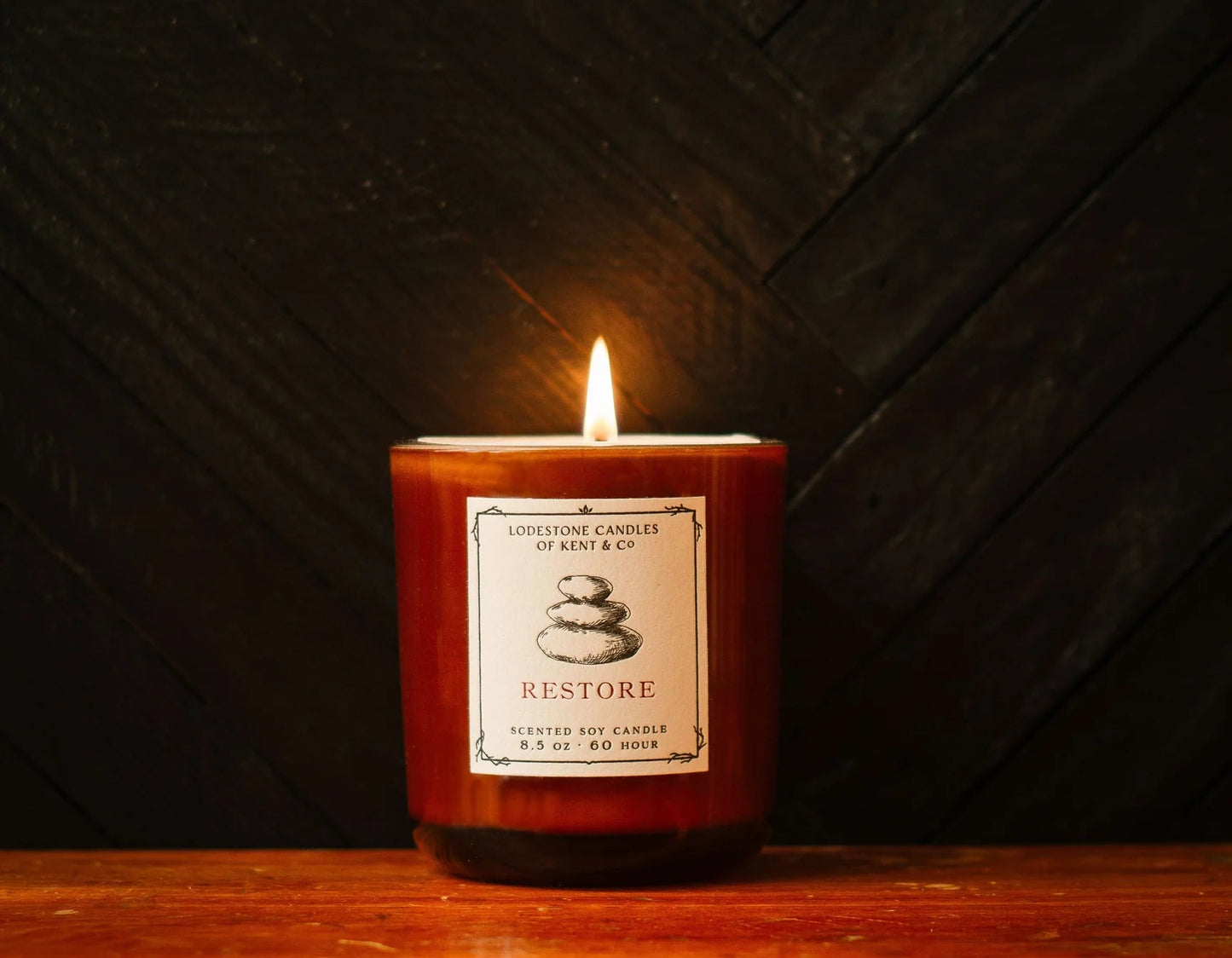 Restore soy candle in red glass jar, lit wick, white label on front.