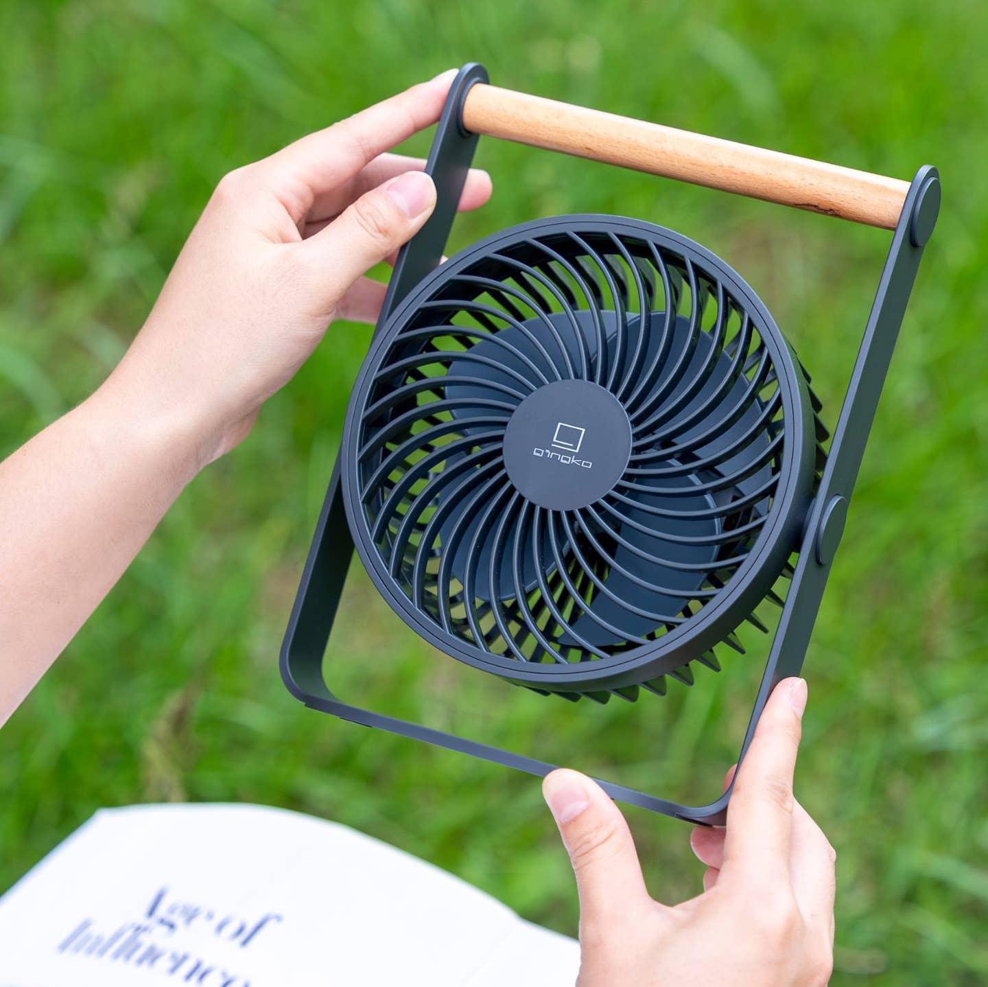 Portable dark fan with wooden handle, circular grille and frame held in hands