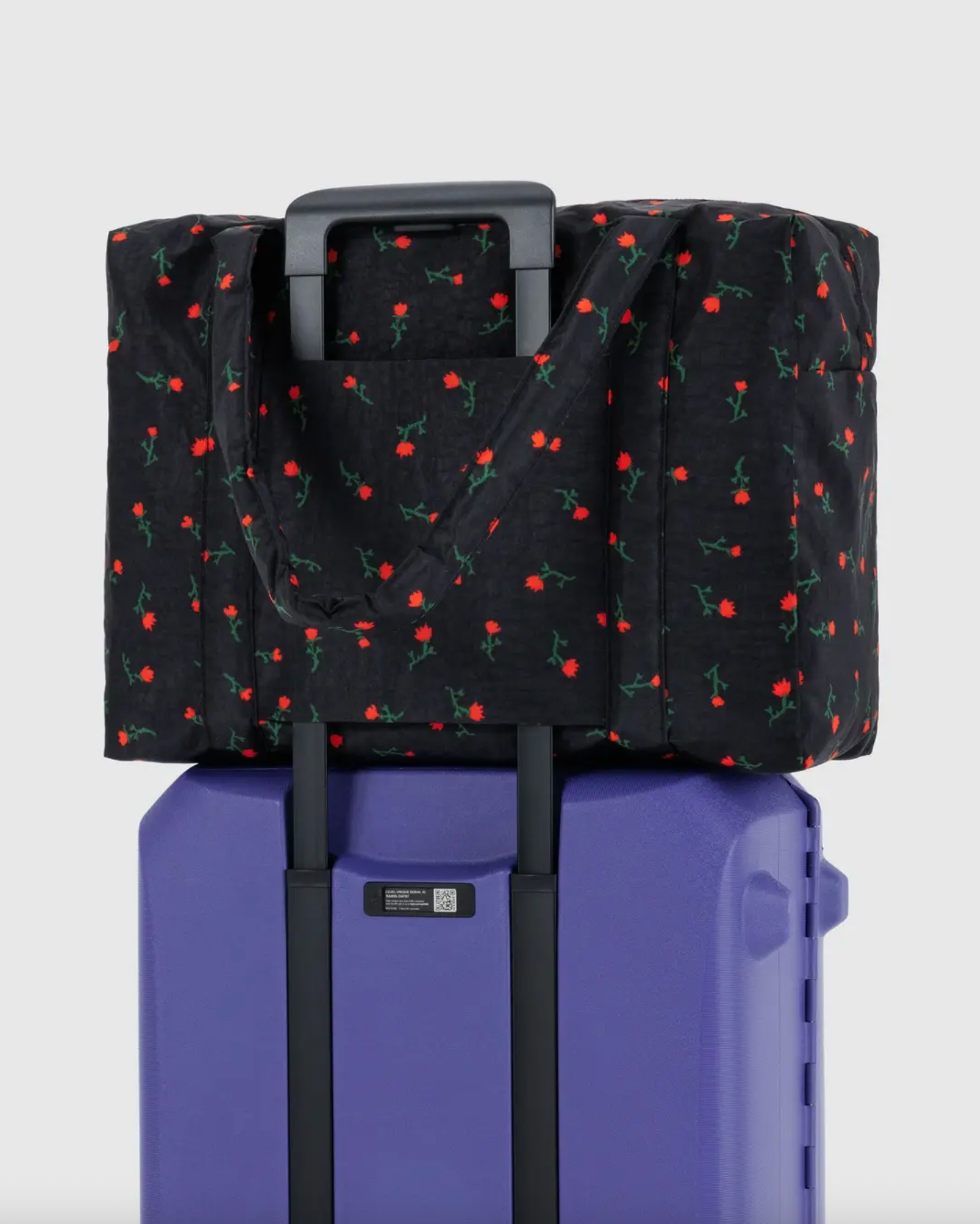 Cherry print carry-on bag with black exterior fitted over a rolling suitcase handle.