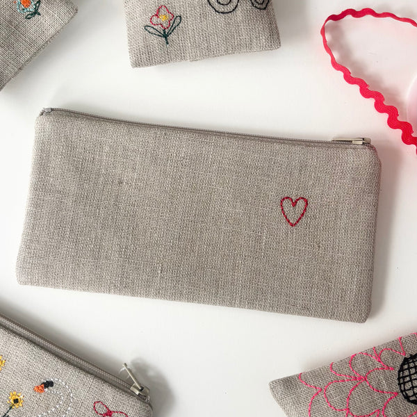 Small gray linen pouch with embroidered red heart detail and zip closure
