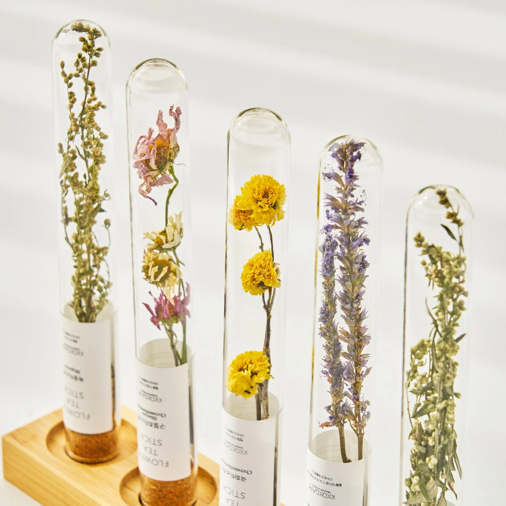 Set of clear flower tea stick vials with dried blooms, standing in a wooden tray