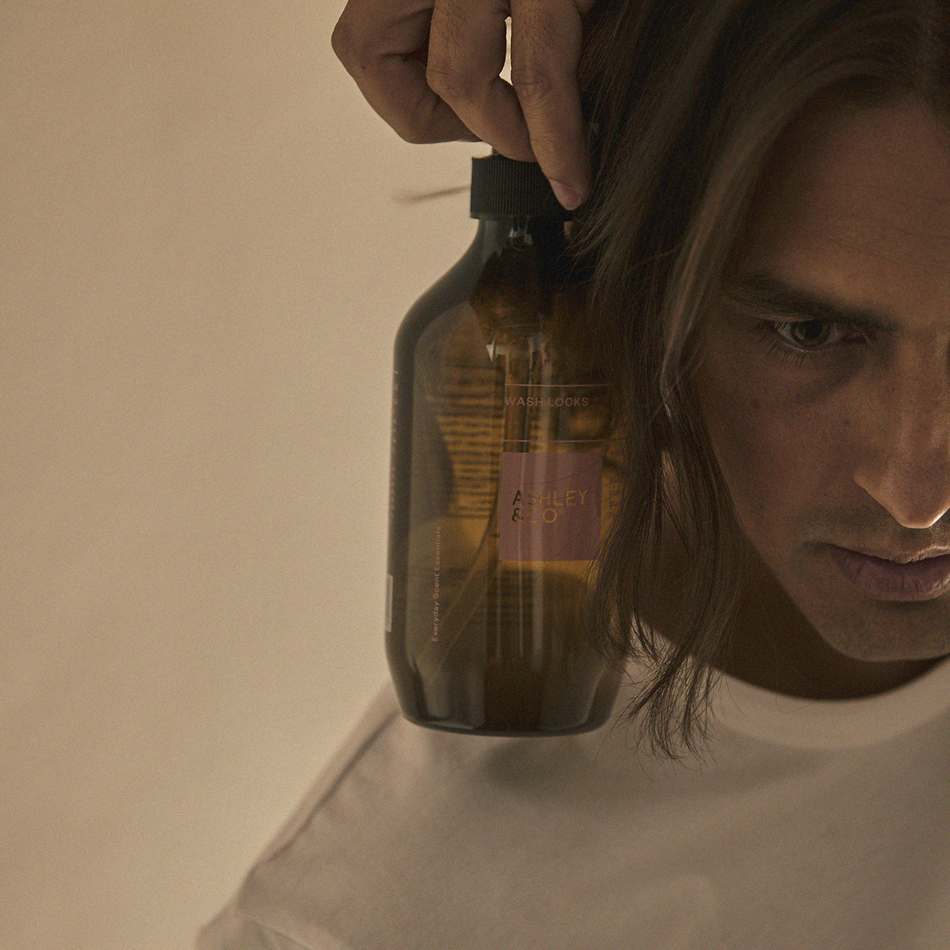 Brown shampoo bottle dispensing into hair, black pump in hand