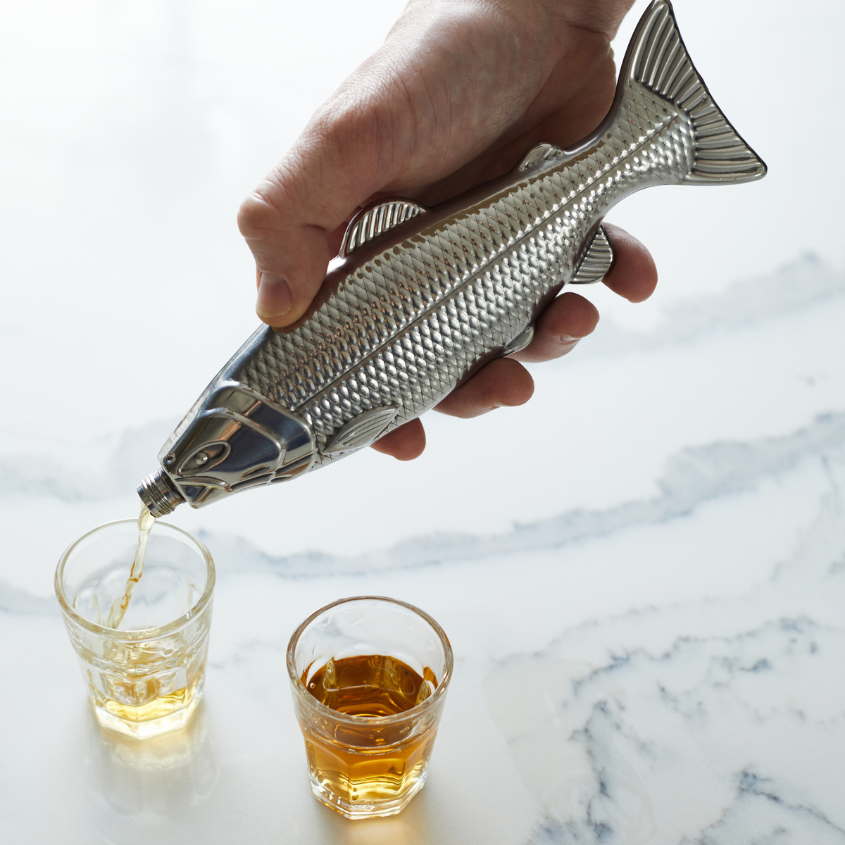 Silver fish hip flask in hand with textured scales and flip-top drinking spout