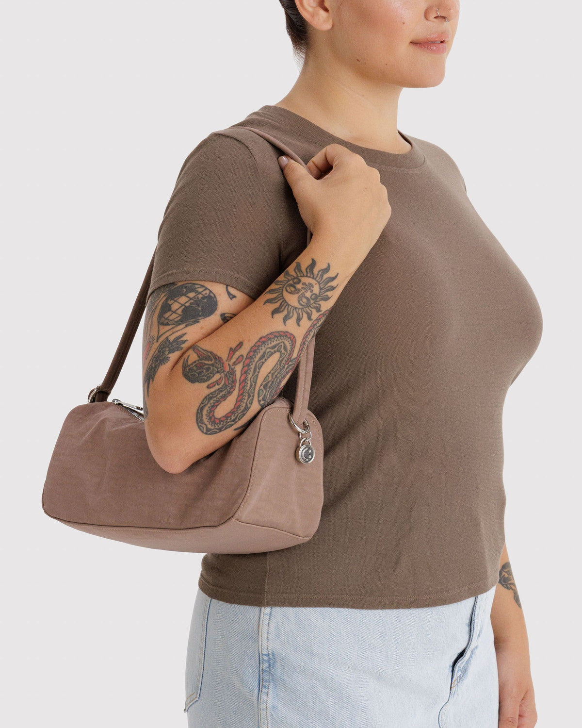 Toasted almond nylon loaf bag worn over shoulder; curved handle and top zipper.