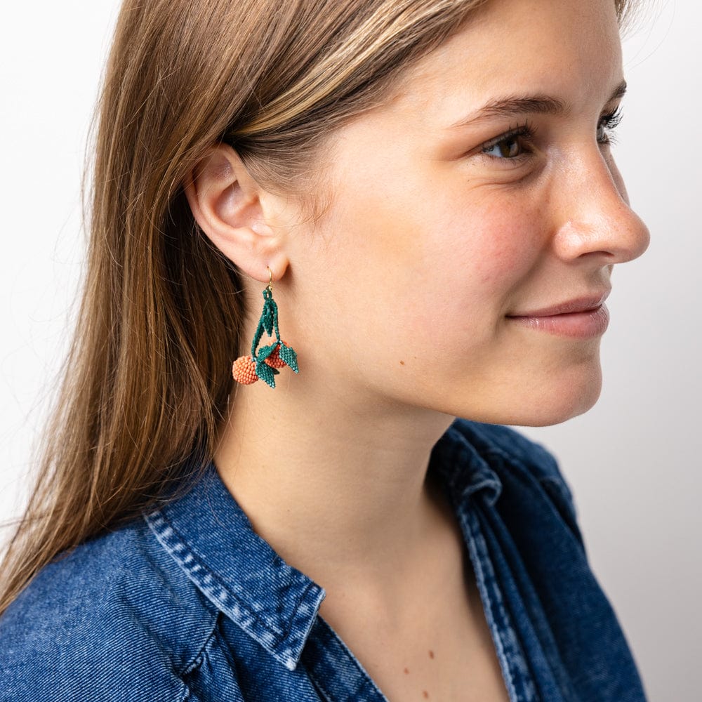 Beaded dangle earrings worn, green leaf shapes with orange bead accents