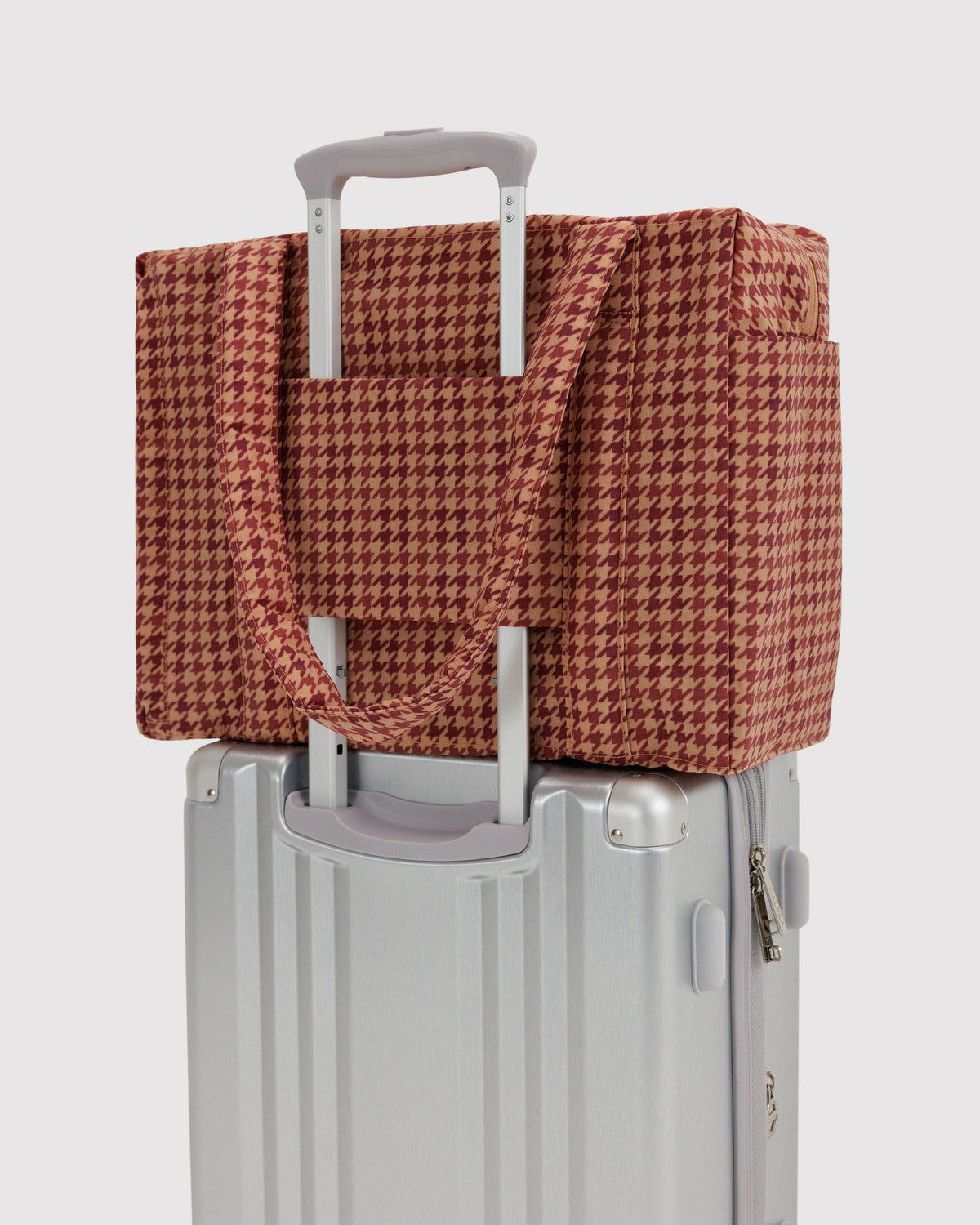Brown and tan houndstooth tote bag secured on a rolling suitcase with luggage strap.