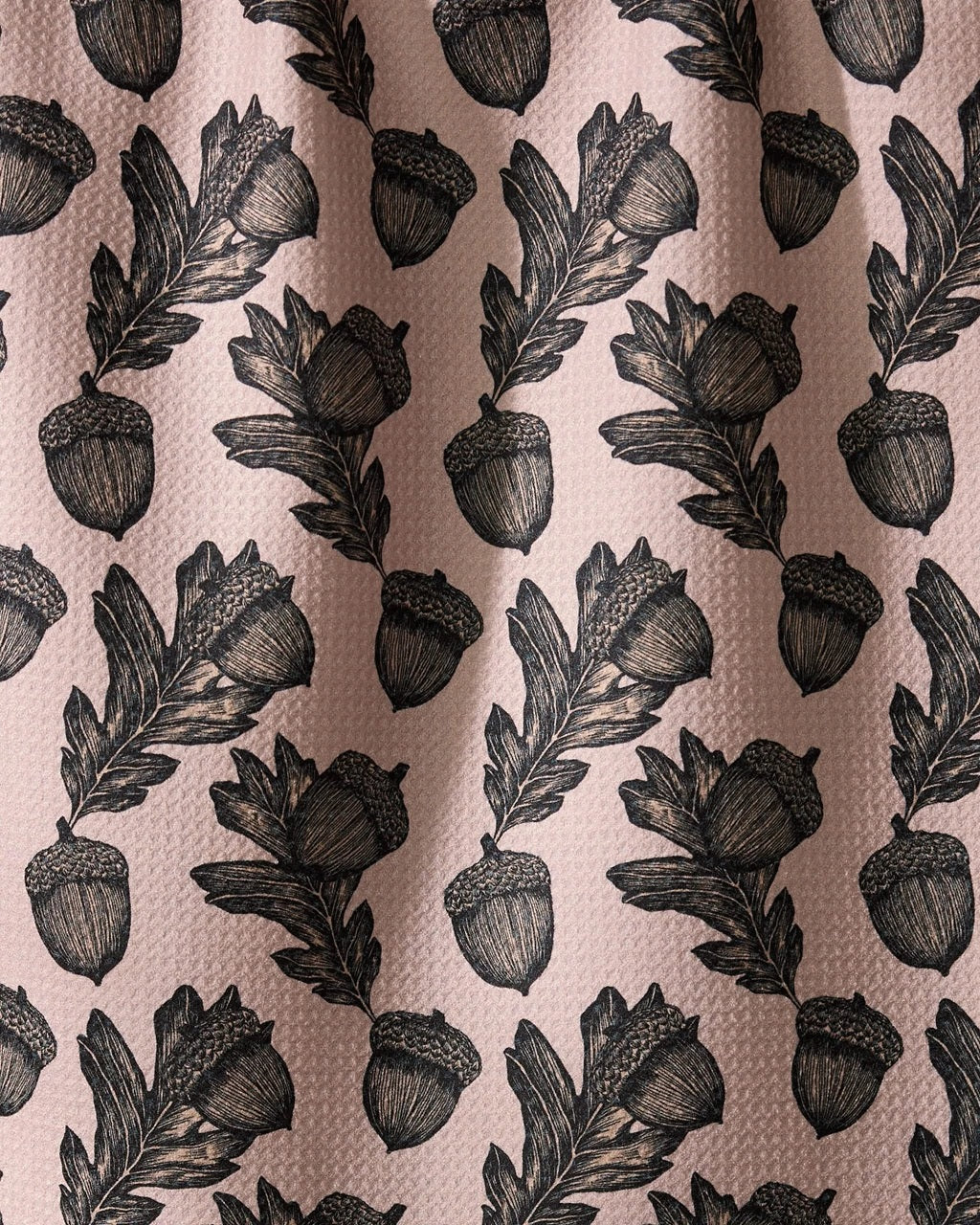 Pink kitchen tea towel close-up with black acorns and leafy sprigs pattern