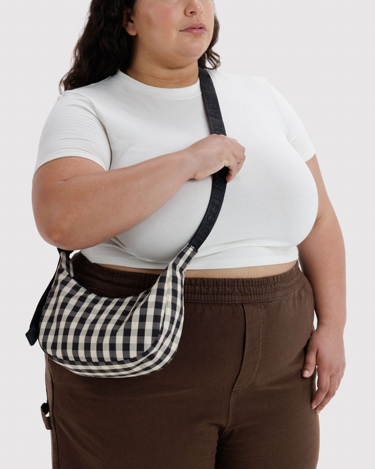 Small nylon crescent bag in black and white gingham worn crossbody