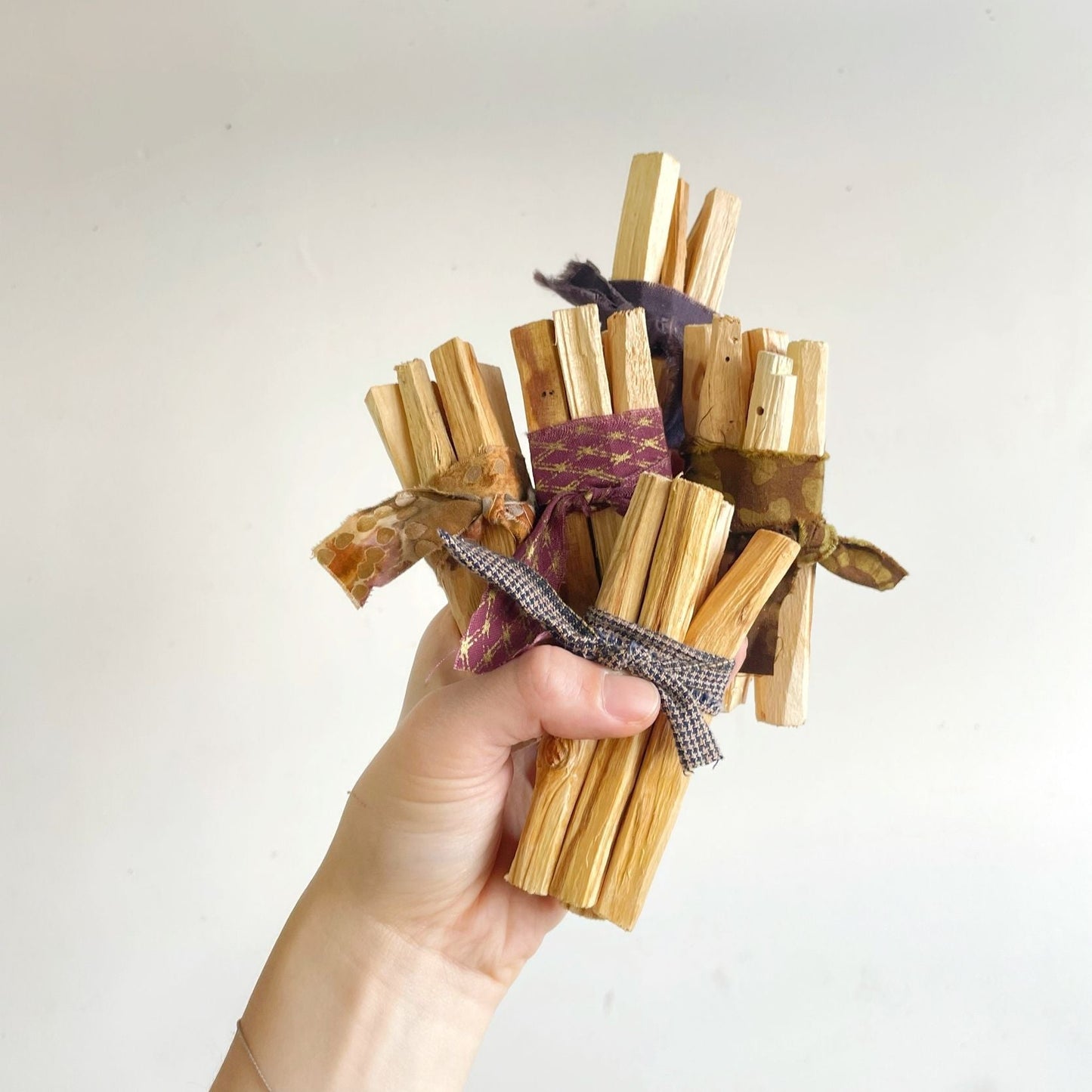 Palo Santo bundle of tied incense sticks, held in hand with twine ribbon